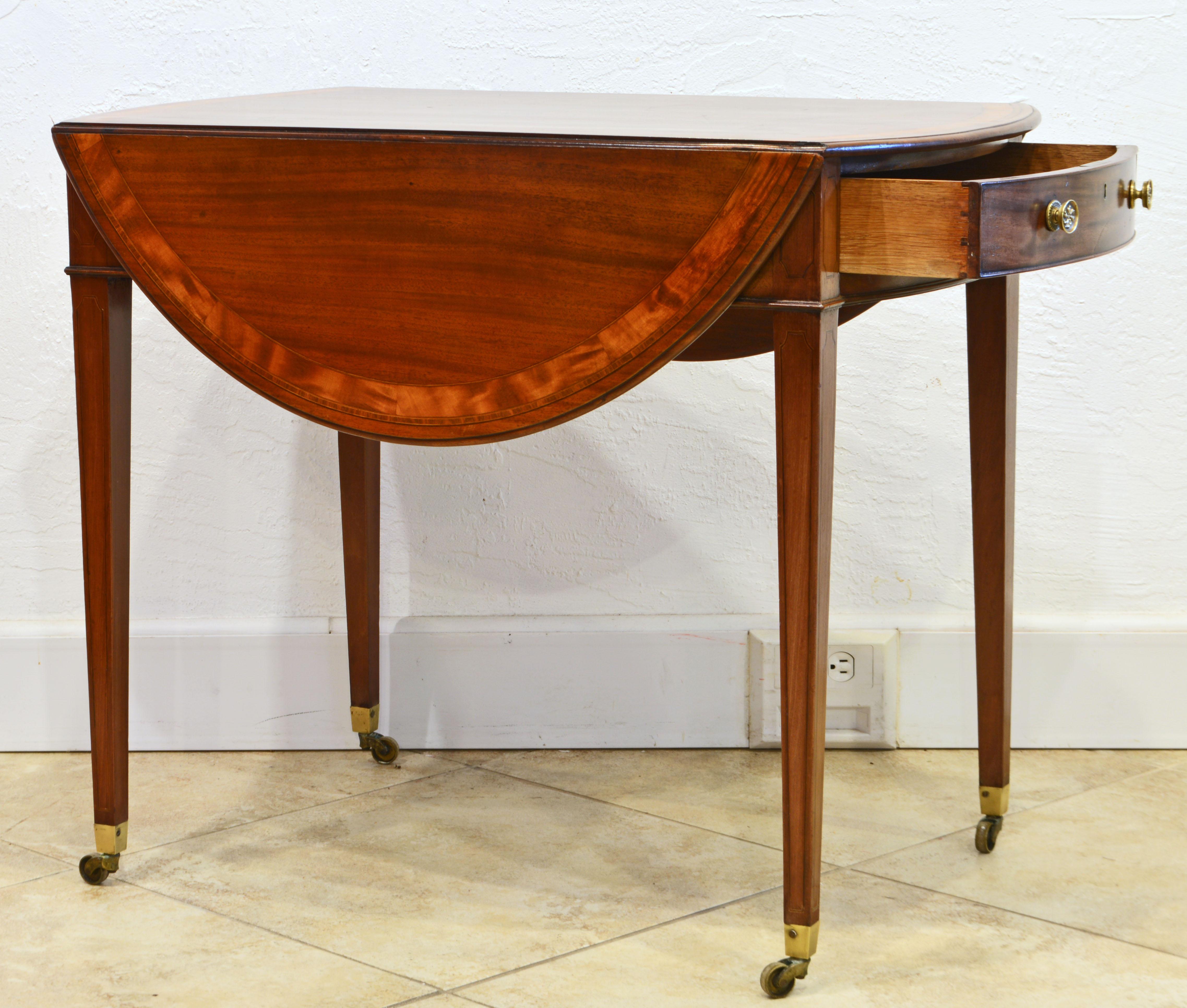 This distinguished George III inlaid and banded mahogany Pembroke table has drop leaves on both sides opening up to a very useful oval shape table. The drawer has one drawer and a meticulously simulated drawer front on the opposite end. The table
