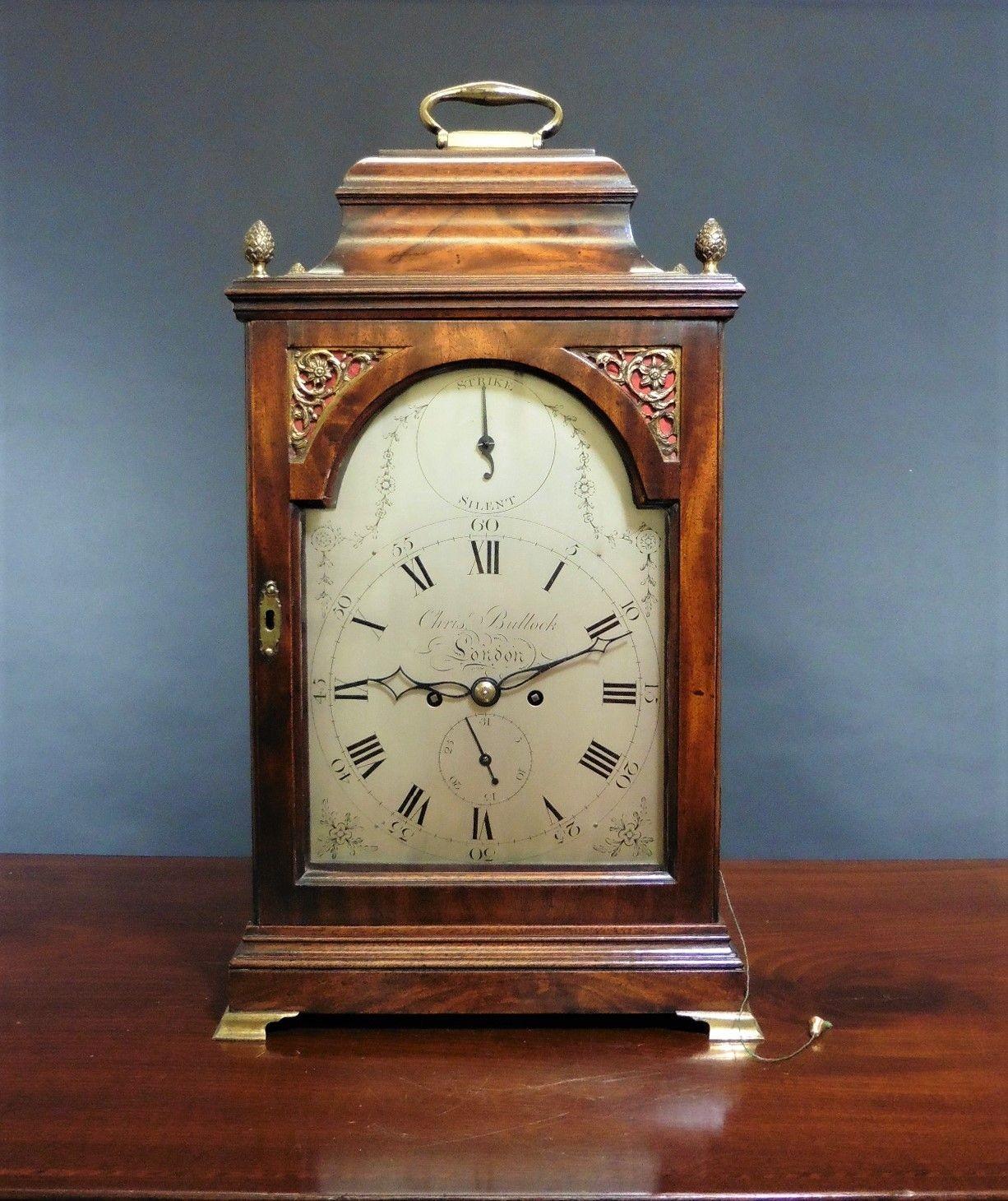 George III bracket clock by Christopher Bullock, London

Finely figured mahogany bell top case with four ‘pineapple’ finials surmounted by a hinged carrying handle standing on a stepped, raised plinth and resting on four outswept brass bracket feet.