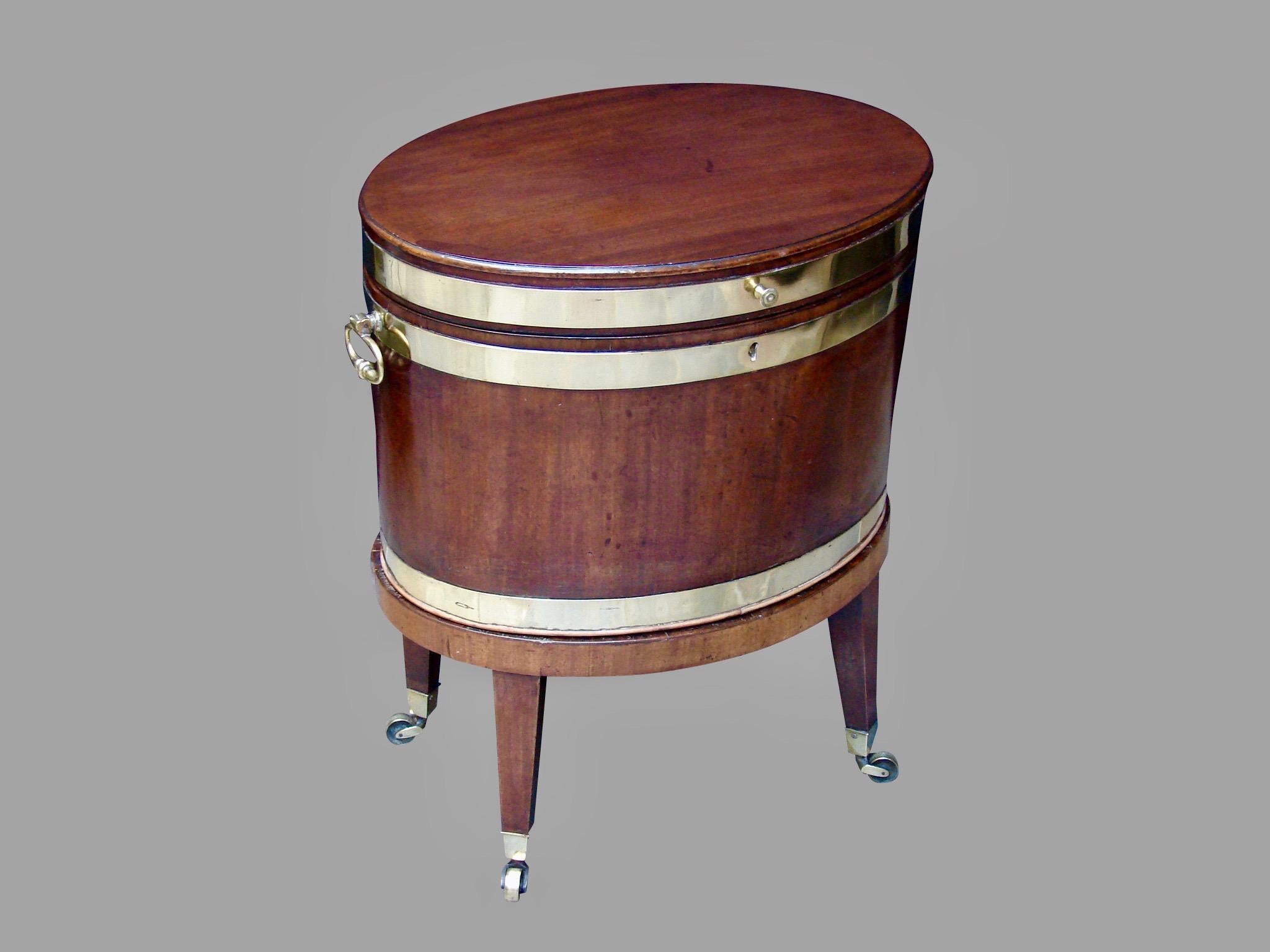 A George III mahogany brass-banded oval cellarette with side carry-handles, retaining its original stand with square tapered legs ending on casters, circa 1790.