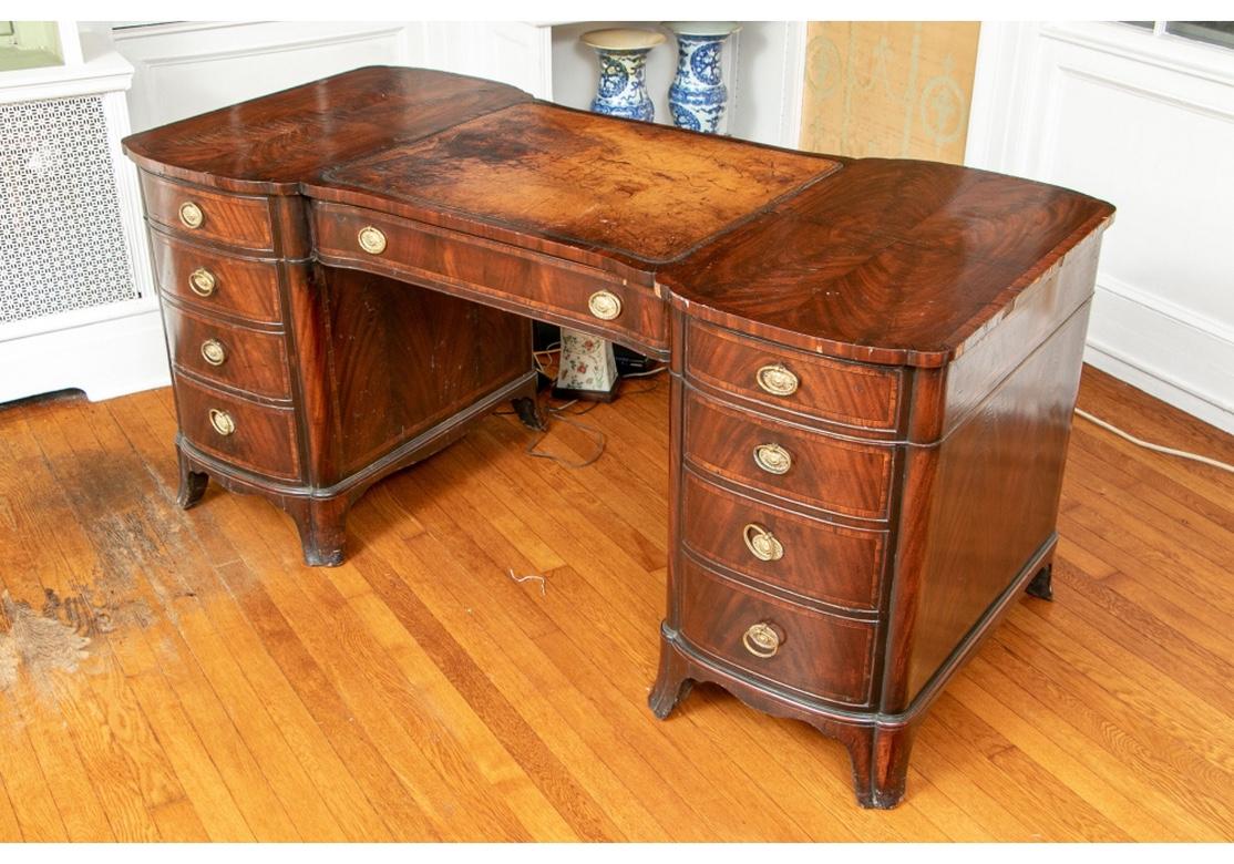 A finely crafted shaped banded burled desk with drawers on both the front and back. The top has bookmatched burled panels on the sides flanking a tan tooled leather center. The side supports have four graduated banded and burled drawers each, with