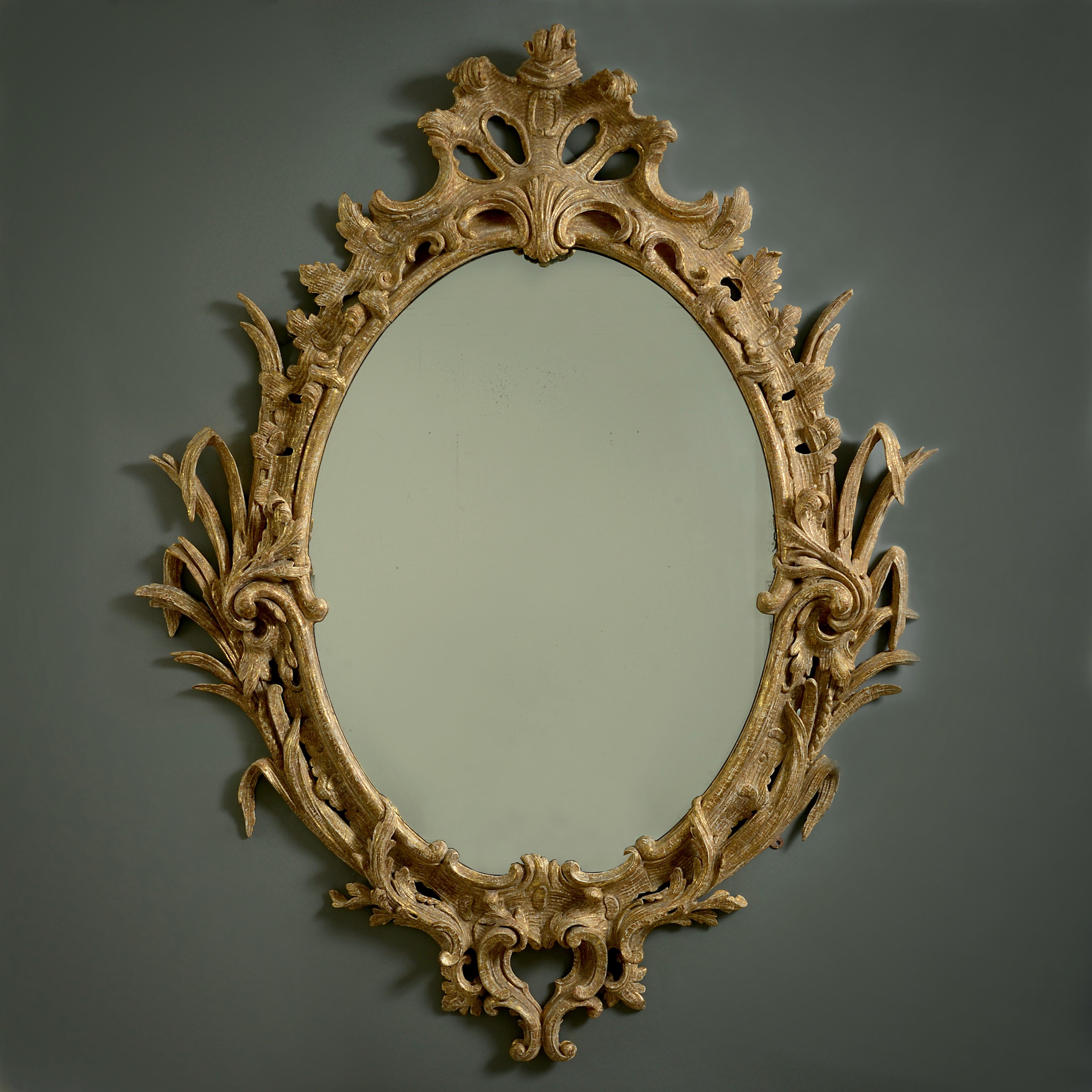 A fine George III carved gilt-wood oval mirror, circa 1765.

The pierced frame boldly carved with reeds, scrolls and rocailles. The oval mercury-silvered plate a 19th century replacement.
