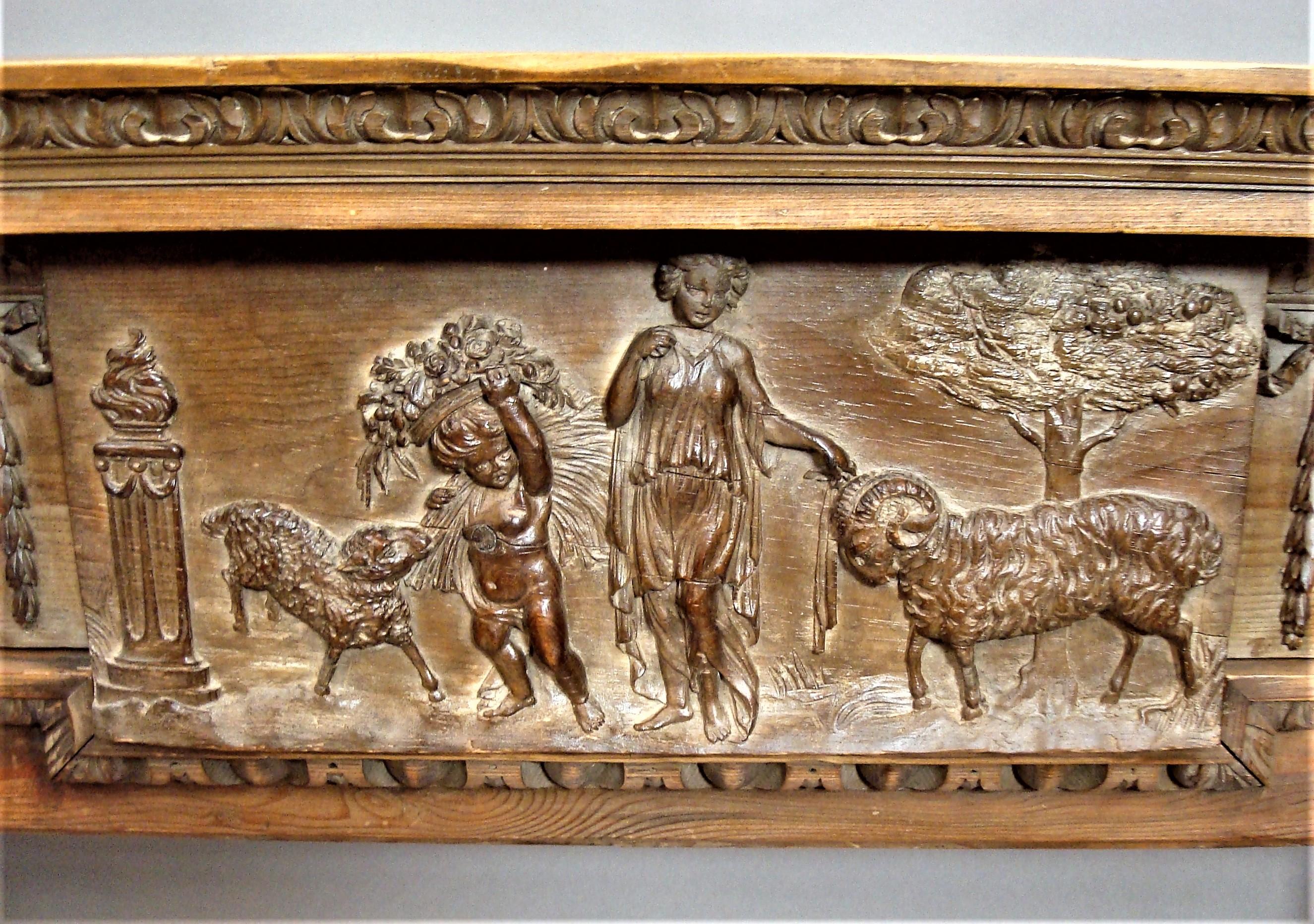 George III carved pine chimney piece / fire surround; the flat mantel (fireplace) shelf of breakfront form with a leaf carved moulding to the underside above the carved frieze with a large central tablet depicting a scene of a classical maiden and