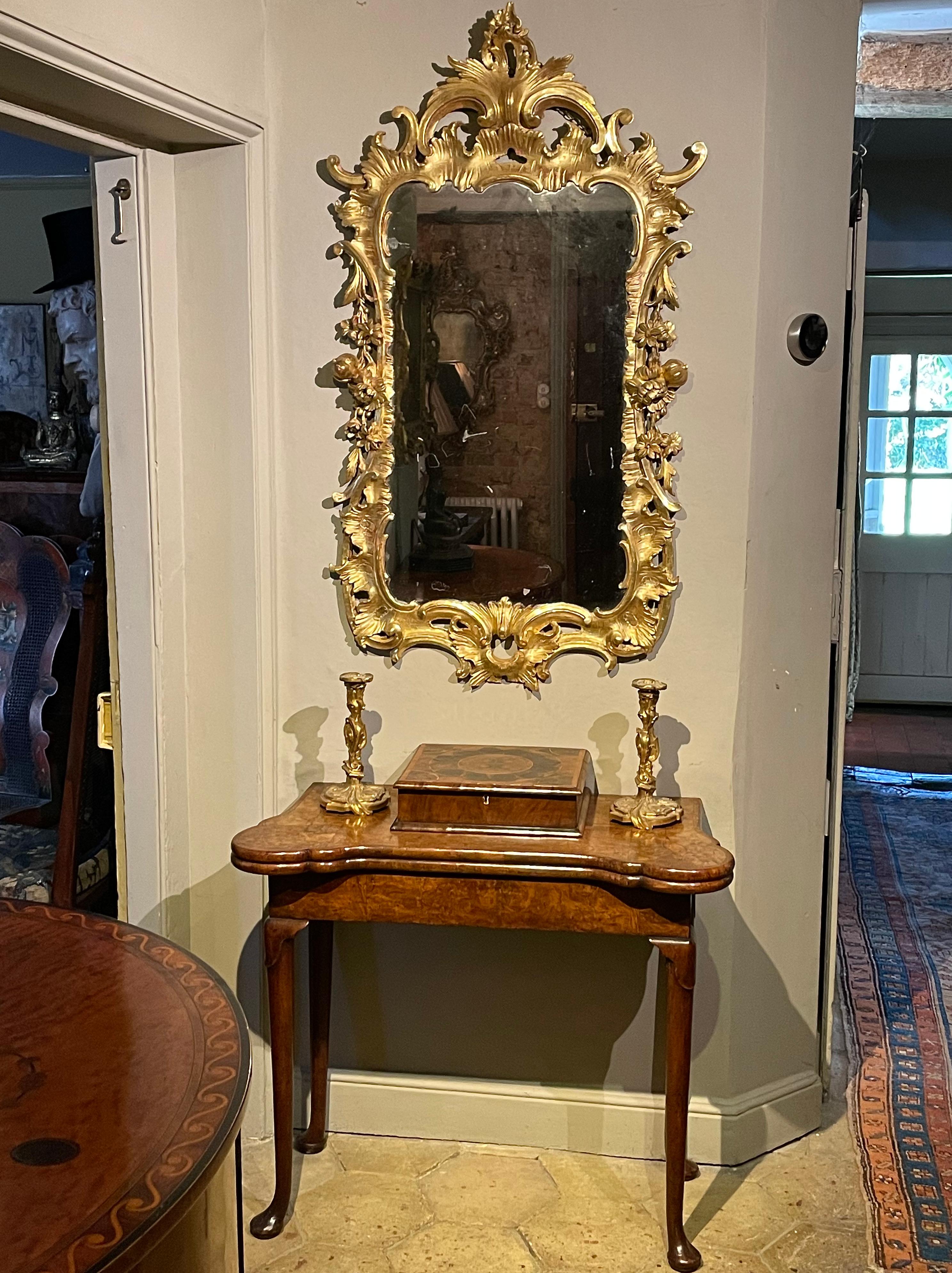 An English Chippendale period carved giltwood mirror, mid-18th century, ca 1755.

Flanked, in a delicately shaped frame, by carved fruit, bold C scrolls and foliage: very typical of this period.
This sophisticated antique mirror dates from the