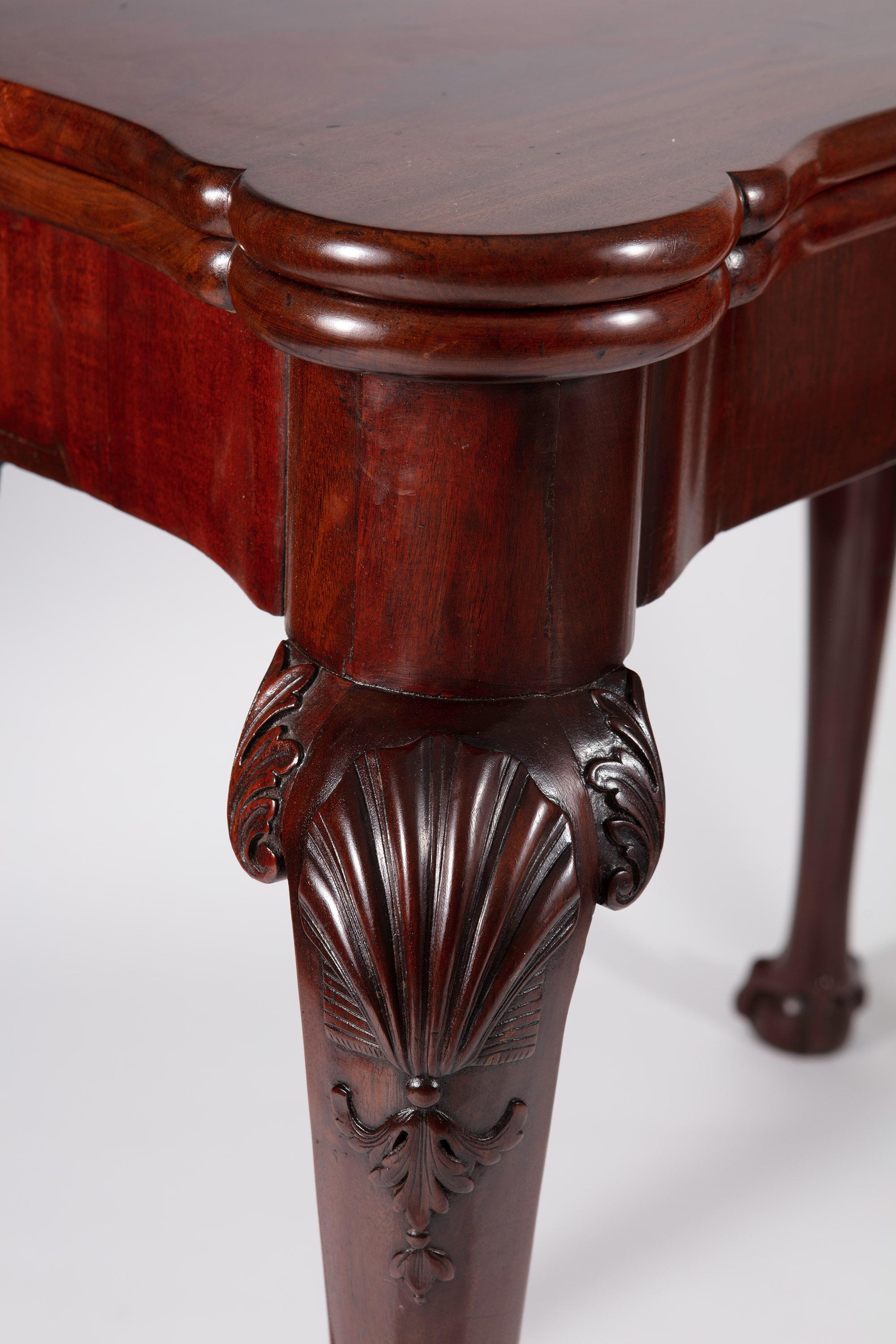 A fine mid-18th-century rich mahogany George III card table raised on cabriole legs with ball and claw feet, scallop shells carved in high relief on all four legs with swags, supporting a folding top opening to baize with sunken counter