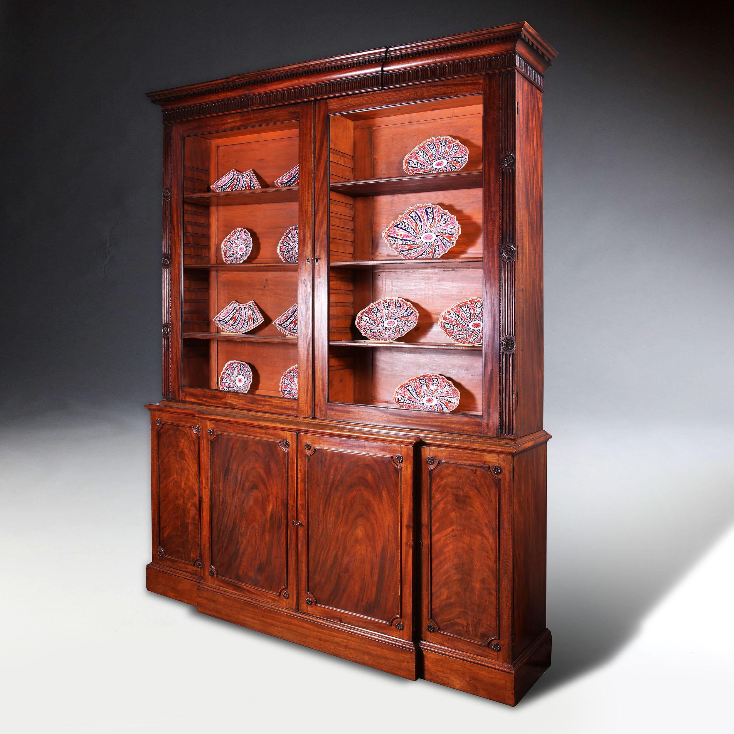 George III Chippendale period mahogany breakfront bookcase.
Having a moulded and dentilled cornice above a fluted frieze, enclosed by a pair of glazed doors flanked by fluted and stop-fluted pilasters carved with paterae, the base enclosed by two