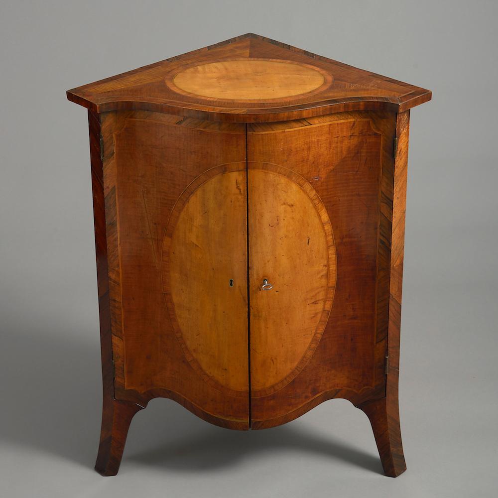 A George III fiddle-back mahogany, satinwood and rosewood bombé corner cabinet attributed to John Cobb, circa 1770.