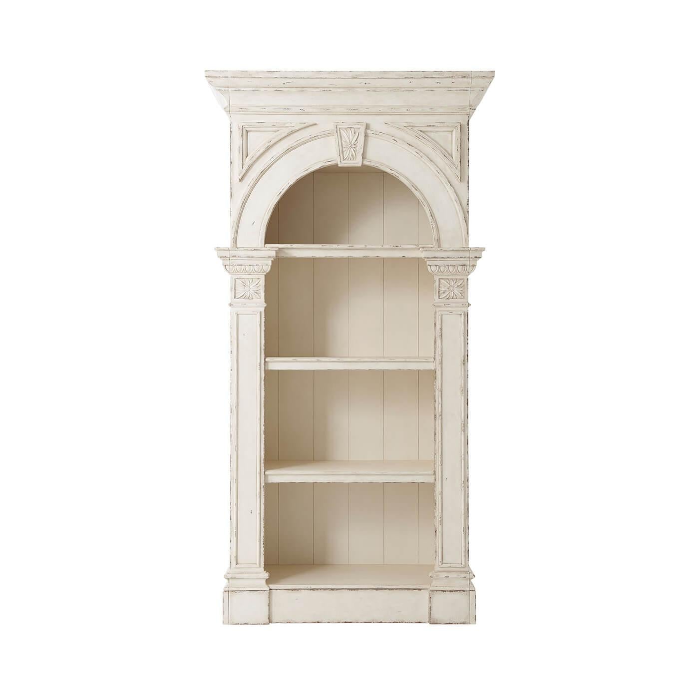 A country house white painted open bookcase, the cavetto cornice above an architectural arch and keystone with column supports enclosing an open interior with LED lighting and a fixed shelf above two adjustable shelves. Inspired by a George III