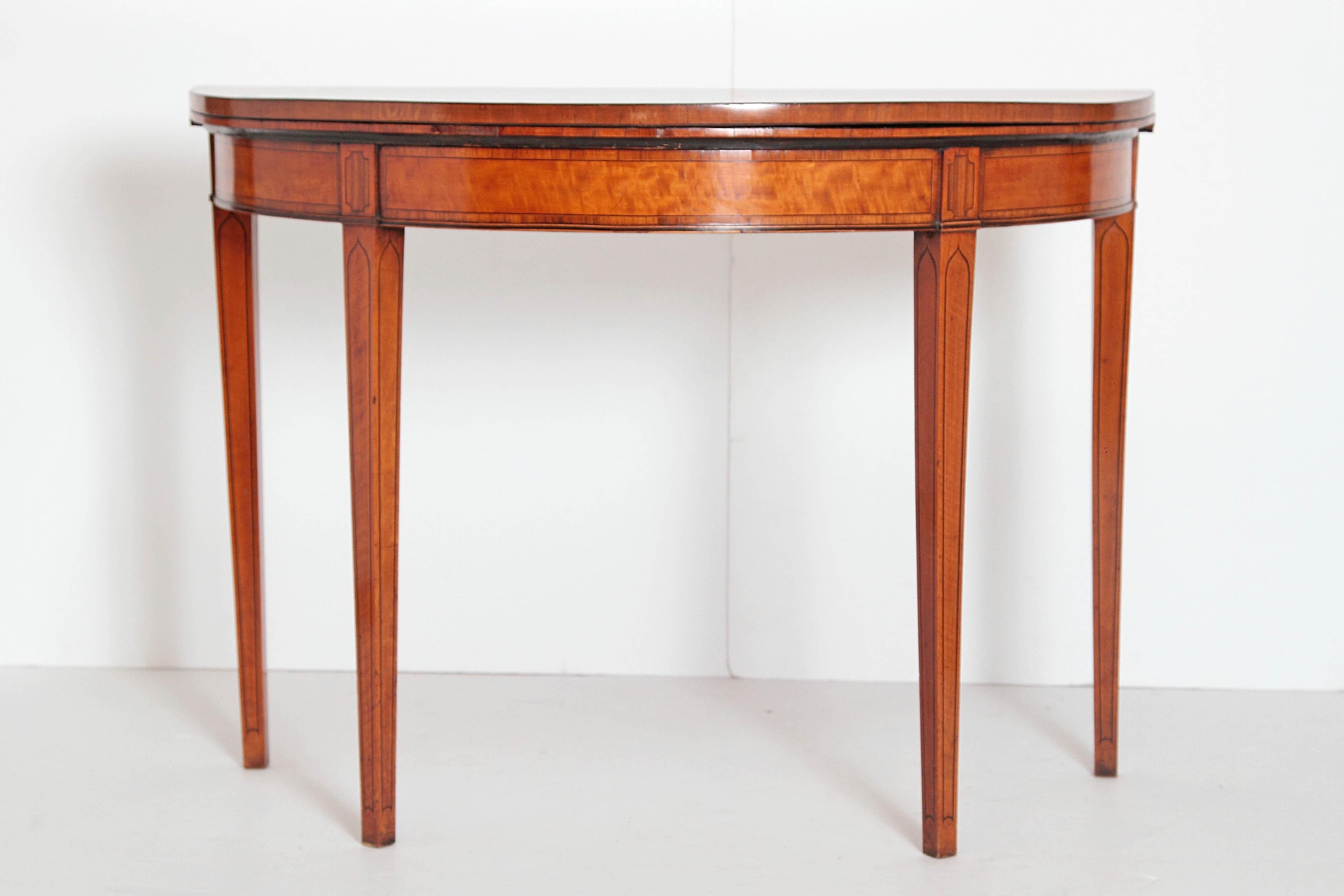 A handsome demilune tea table / games table with crossbanded edge bordering the top. The back legs fold out and the top opens up to a tan suede playing surface. Opens to 38.5