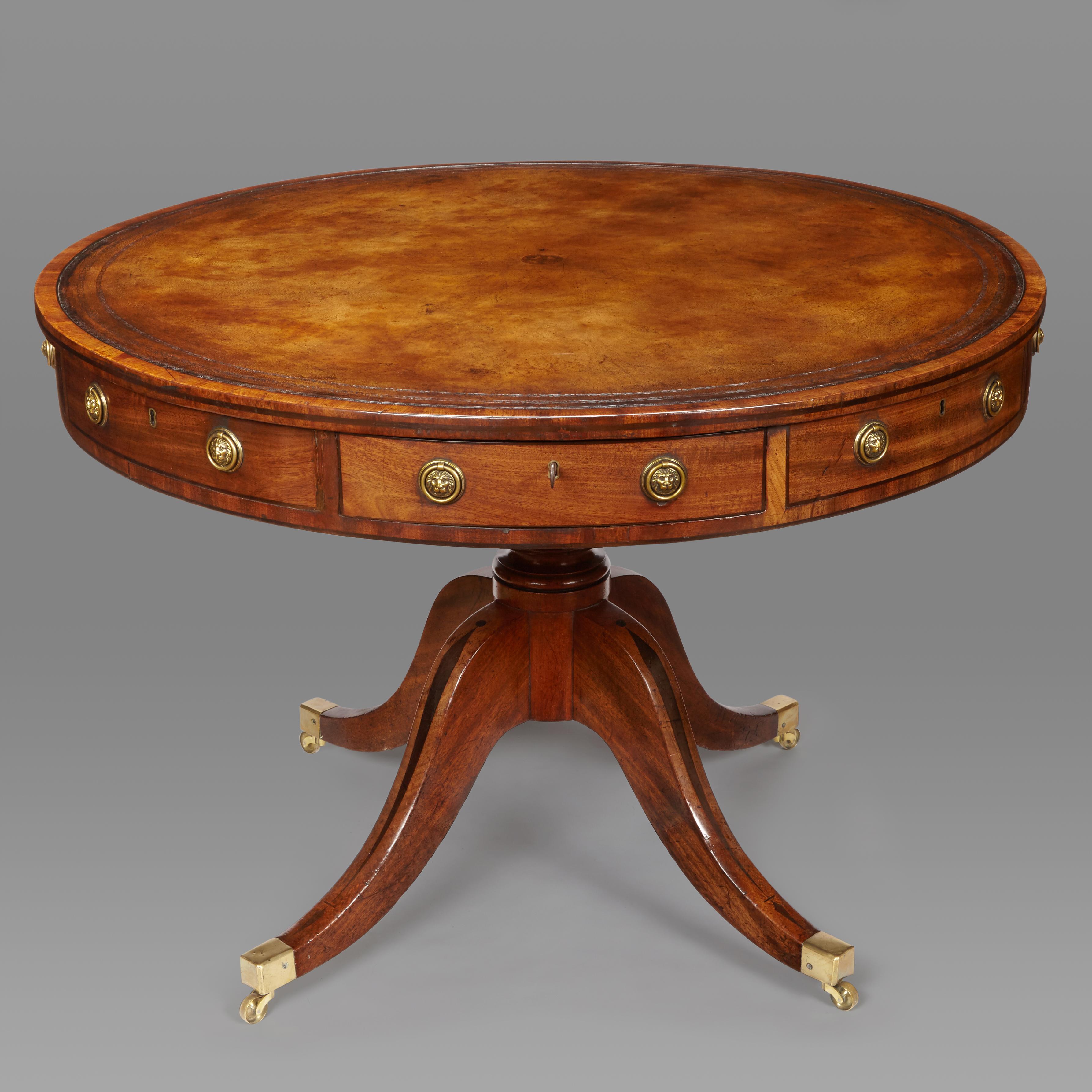 A George III mahogany and ebony inlaid drum table of pleasing proportions. The tan leather inlaid top enclosed by a slim cross- banded edge with ebony line inlay above four oak- lined drawers and four faux drawers fitted with ring handles (old
