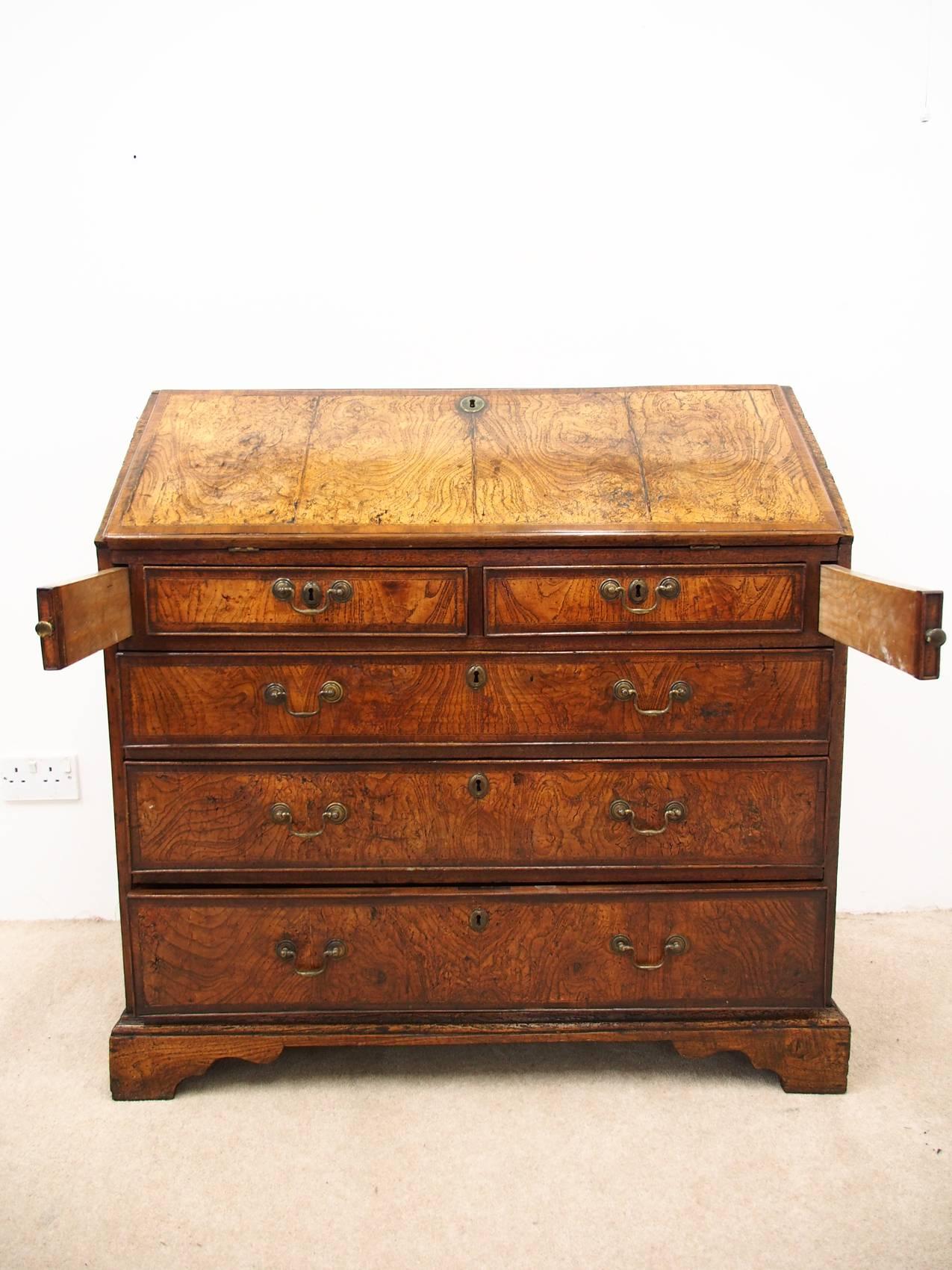 Unusual George III elm bureau, circa 1770. The piece has a beautifully figured elm top with parquetry and cross-banding. It has two smaller drawers, above three larger drawers with brass clip handles. It stands on bracket feet. Beautiful color and