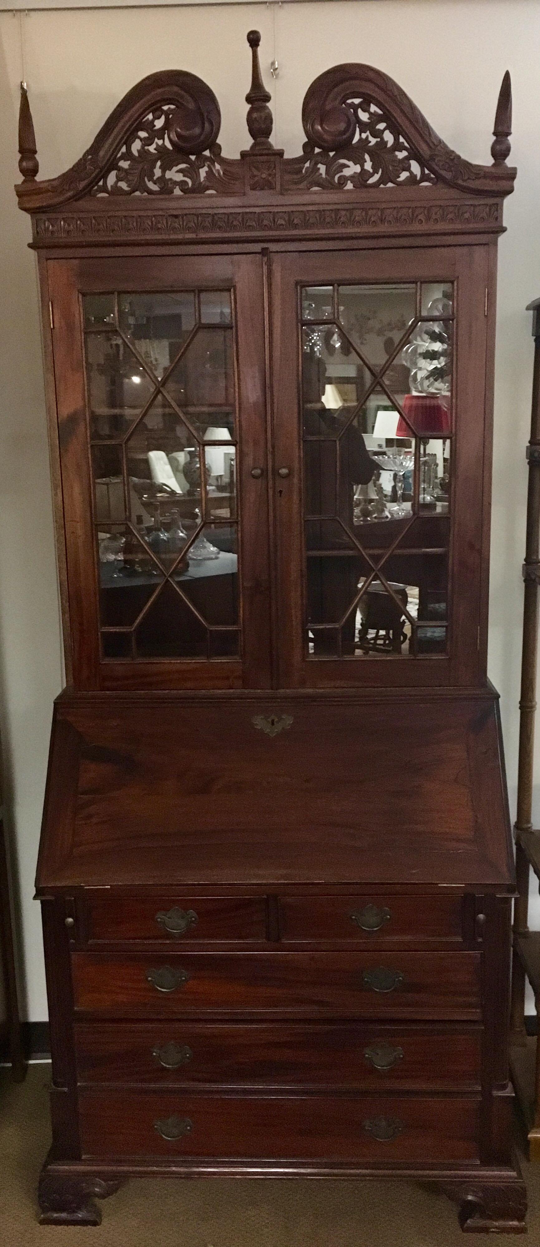 Early George III antique drop front secretary desk with gorgeous detail and multiple drawers and compartments. Features an intricately carved pierced pediment and finials and fretwork ove glass doors.