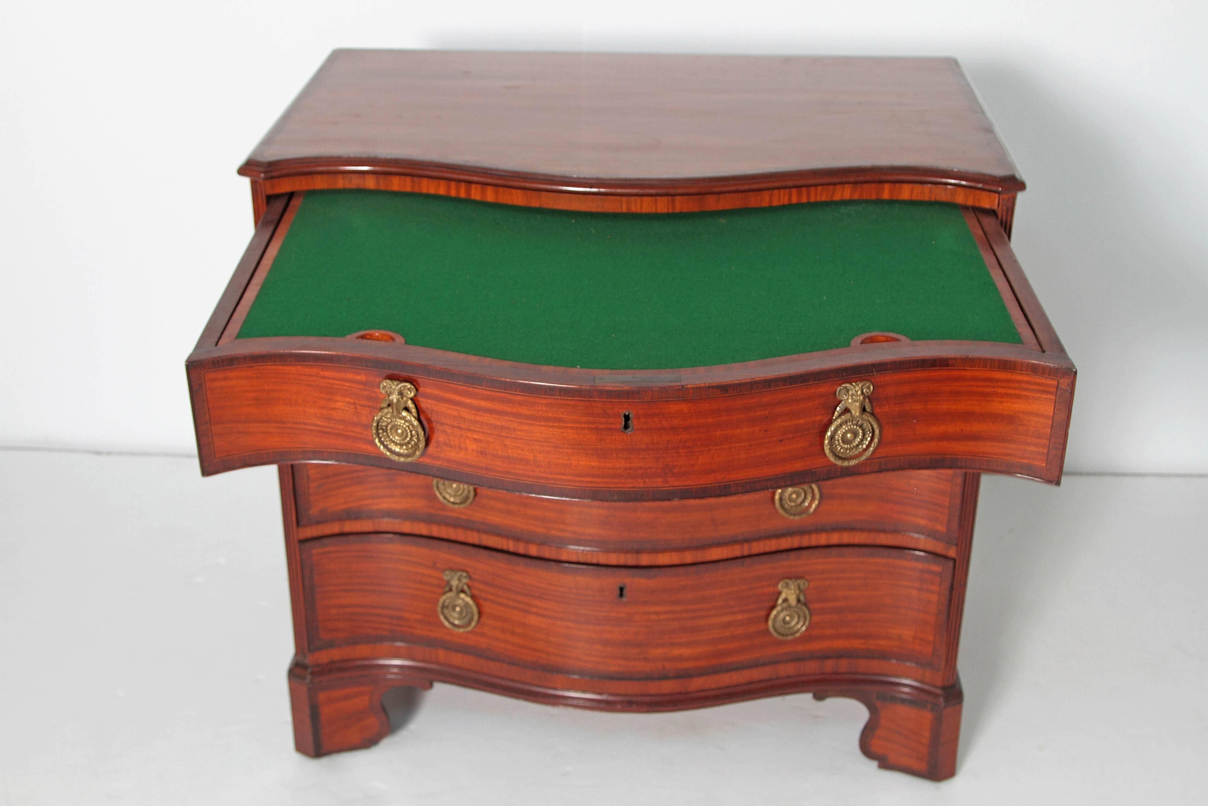 an ingenious and very useful small four-drawer English / Georgian satinwood and mahogany bachelor's chest with serpentine front and inlay around top and drawers, top drawer opens to reveal a baize covered writing slide / work surface with storage