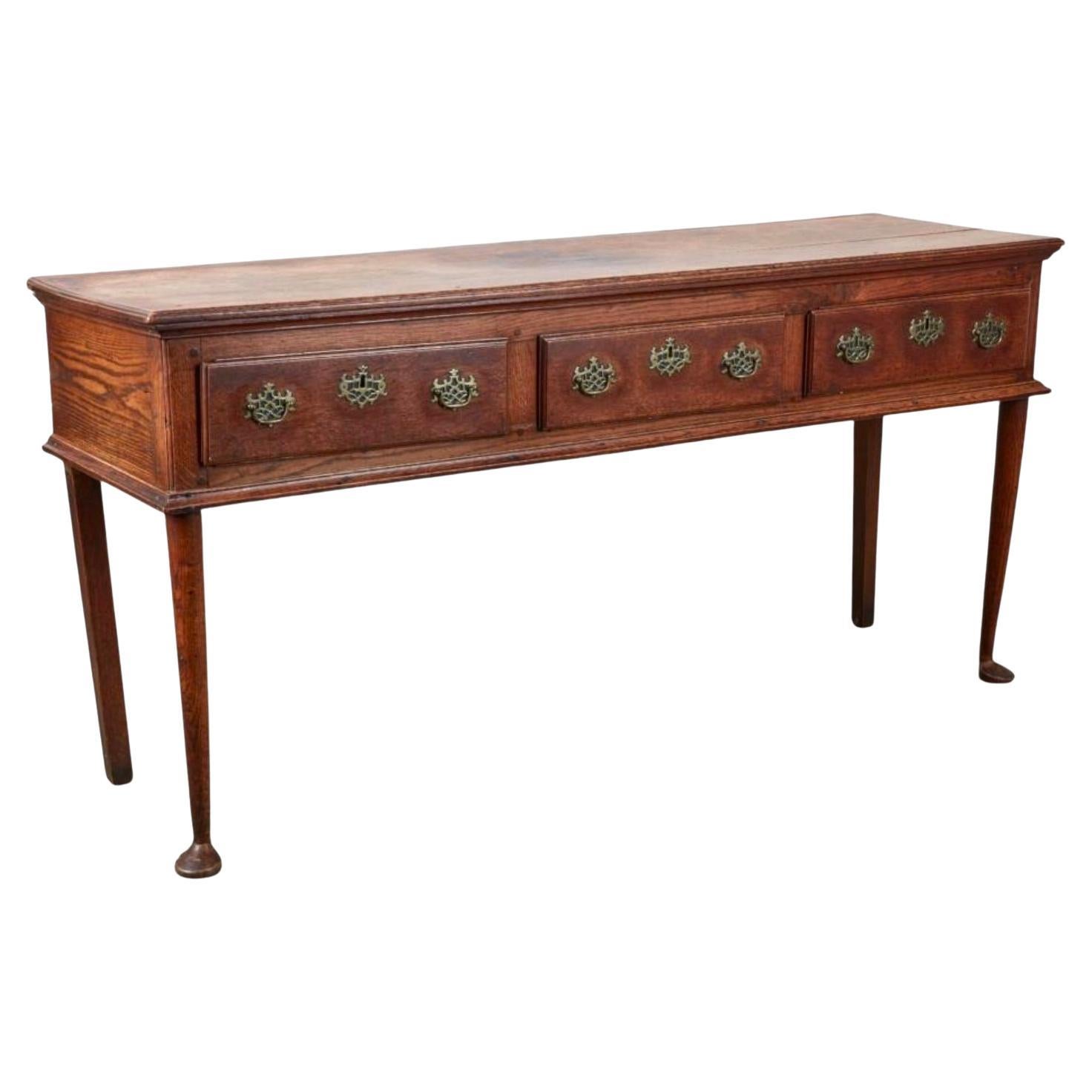 Cómoda/ aparador/consola inglesa de roble Jorge III del siglo XIX, un mueble clásico que encarna la artesanía y el estilo de su época. La cómoda tiene tres cajones espaciosos con herrajes de latón y patas cabriolé que contribuyen a una silueta
