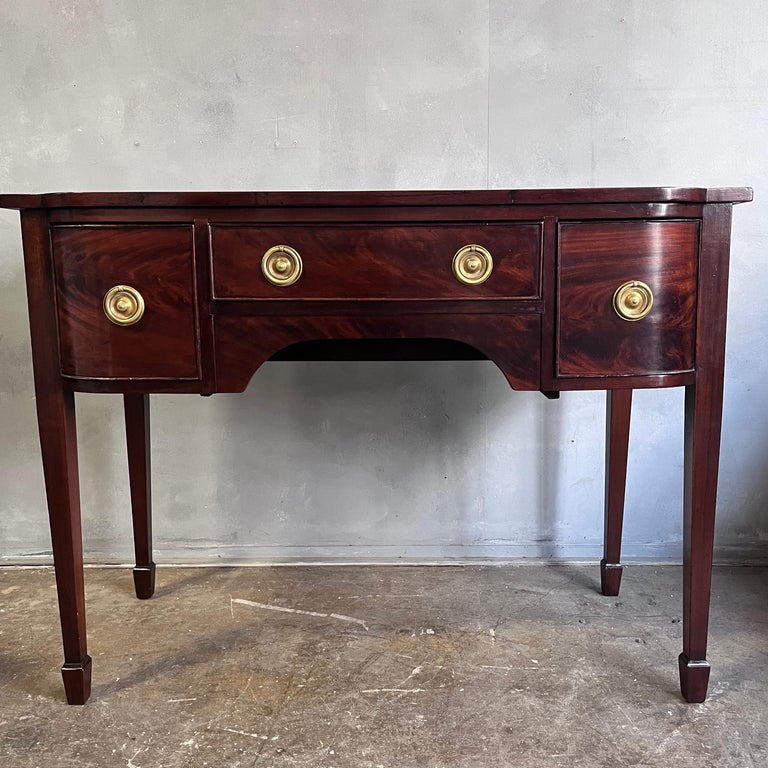 Georgian Hondurian mahogany bow front sideboard and server. Beautiful dark brown color with an old surface. Strong brass ring pull hardware. Tall Hepplewhite legs terminating on spade feet. Good medium scale with balance and proportion. A middle