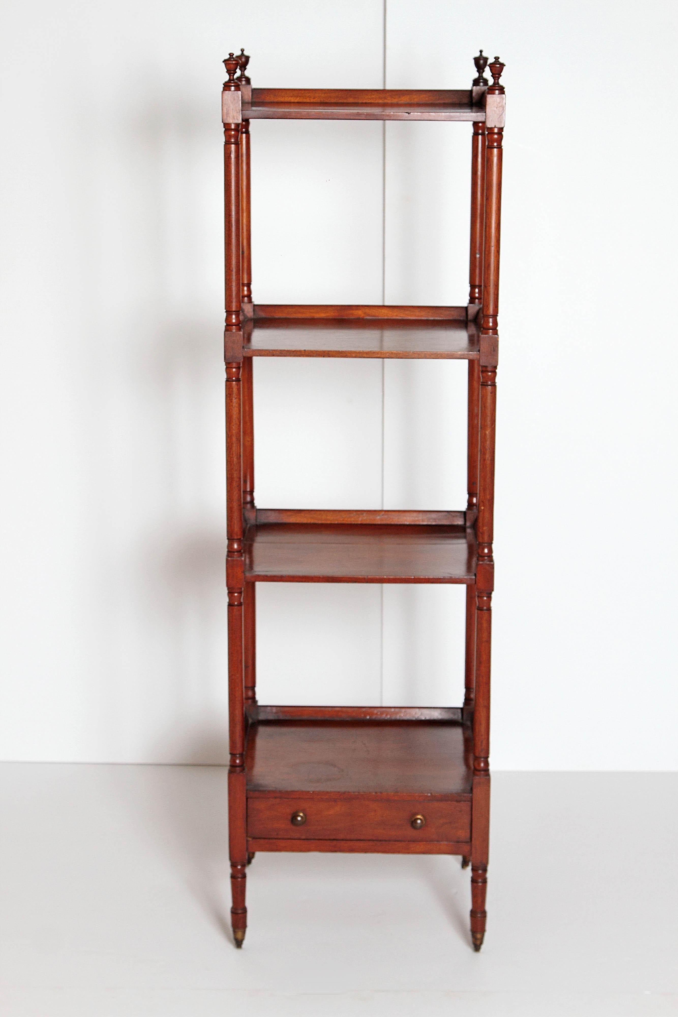 An English Georgian four-tier whatnot with a drawer. The slender turned and baluster shaped supports terminating with urn finials to the top and brass castors to the legs, the bottom tier with a single drawer with wooden knobs, early 19th century,