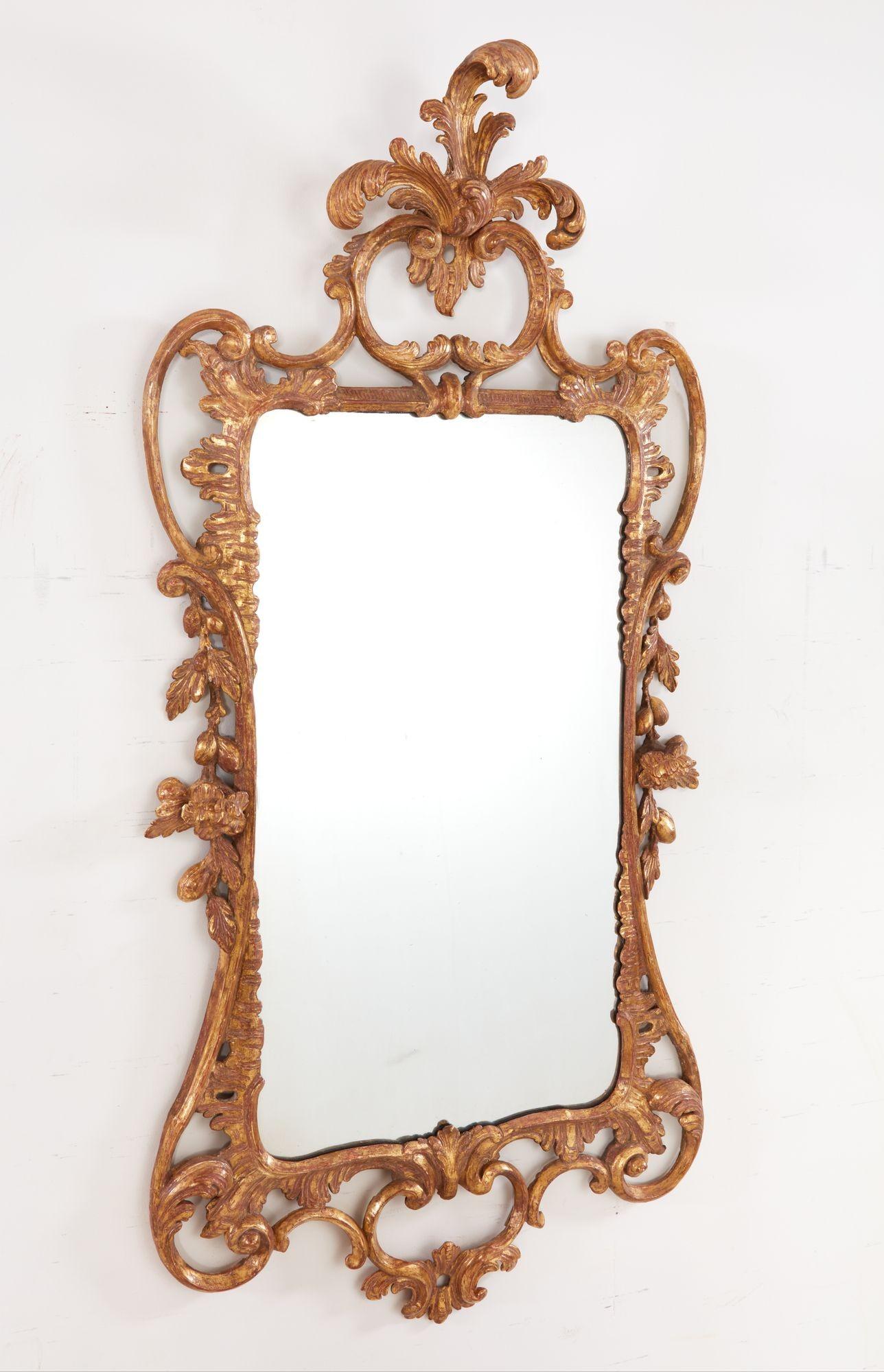 Specchio rettangolare di George III in legno intagliato e dorato, con stemma foliato a volute e corpo intagliato a rocaille e volute, i lati fiancheggiati da ghirlande pendenti di frutta e fiori, il tutto con superficie riccamente brunita e dorata