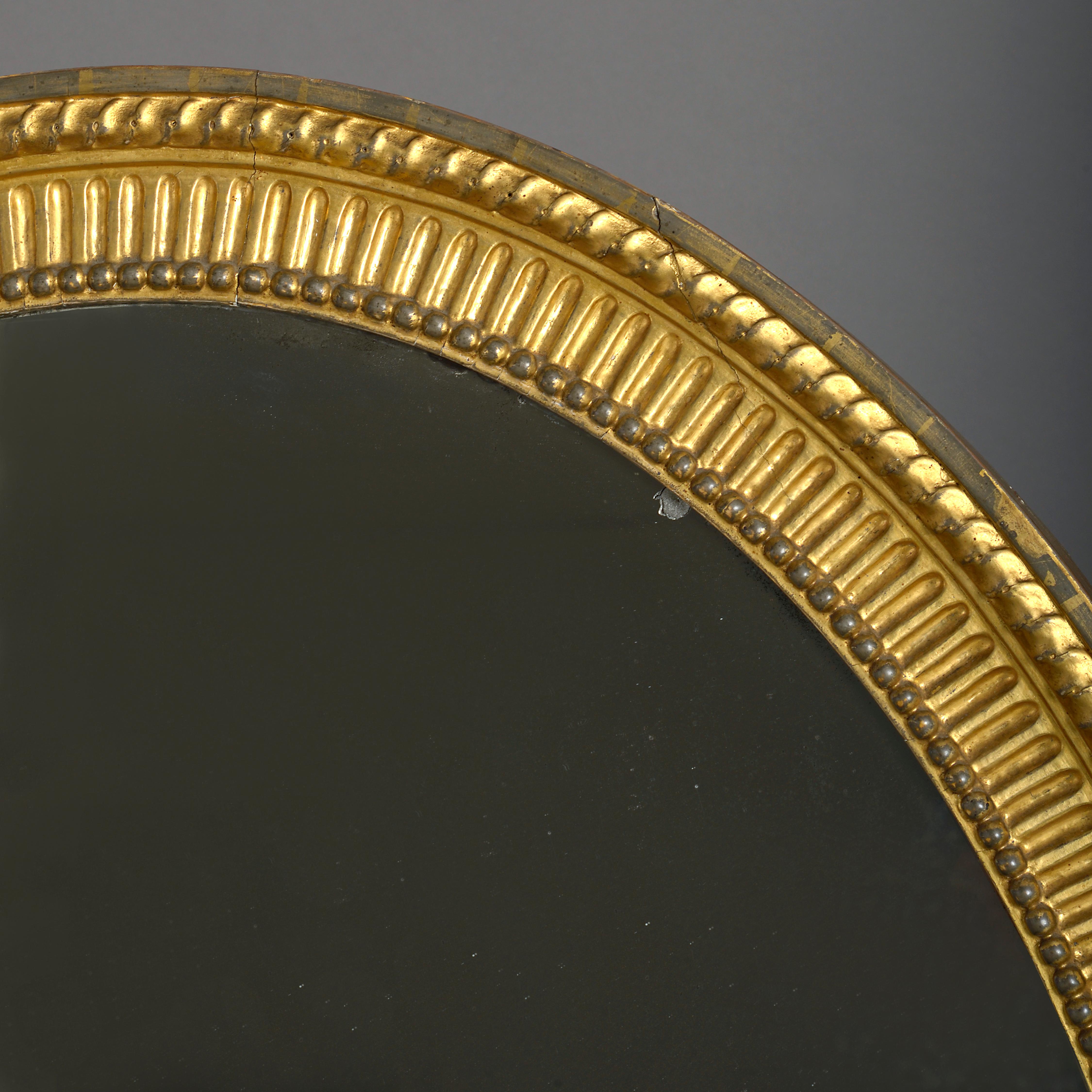 A fine George III carved giltwood oval mirror, circa 1780.

With original plate, the reeded frame carved with guilloche and beads.