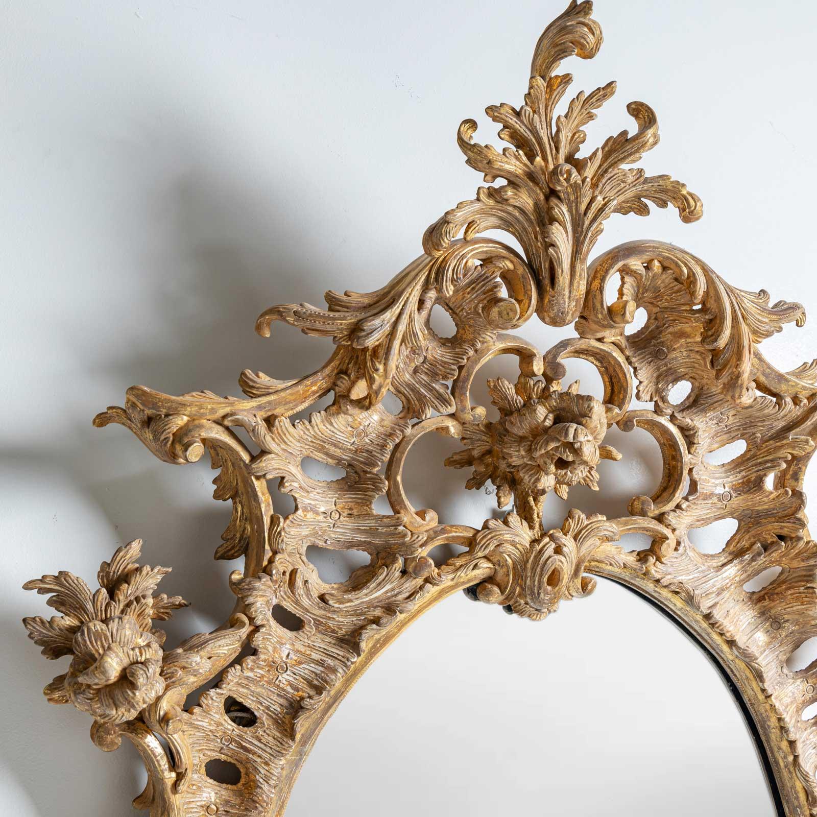 Grande specchio da parete dell'epoca di George III con cornice in legno patinato oro con fibbie a C, decorazioni a rocailles e a rose e uno specchio ovale tagliato. 