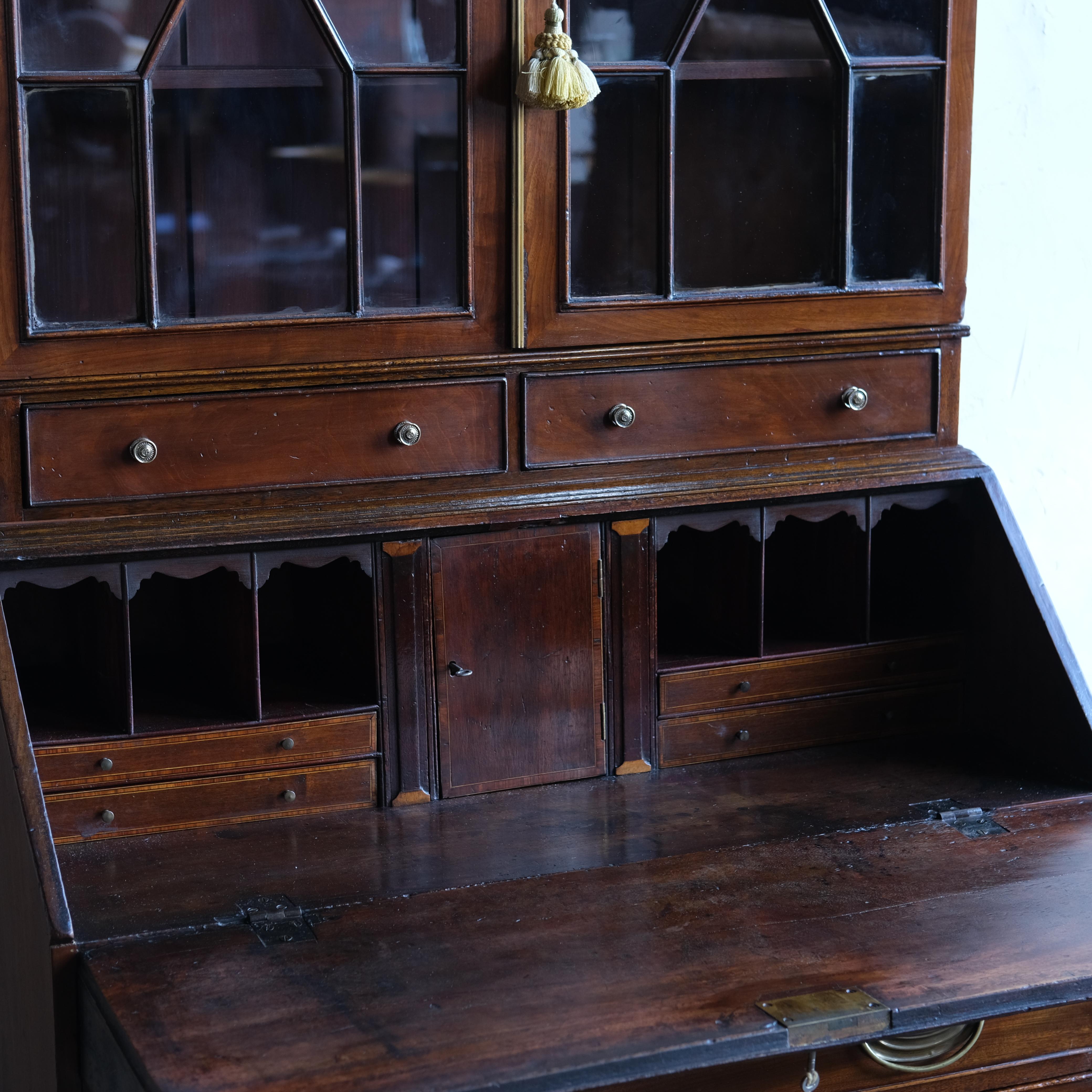 A Georgian mahogany beurau bookcase with 4 long drawers raised on bracket feet. The desk fitted with a delicate interior retaining all its original drawers and keys. The astral glazed top with a broken arch pediment and brass eagle. 

In good