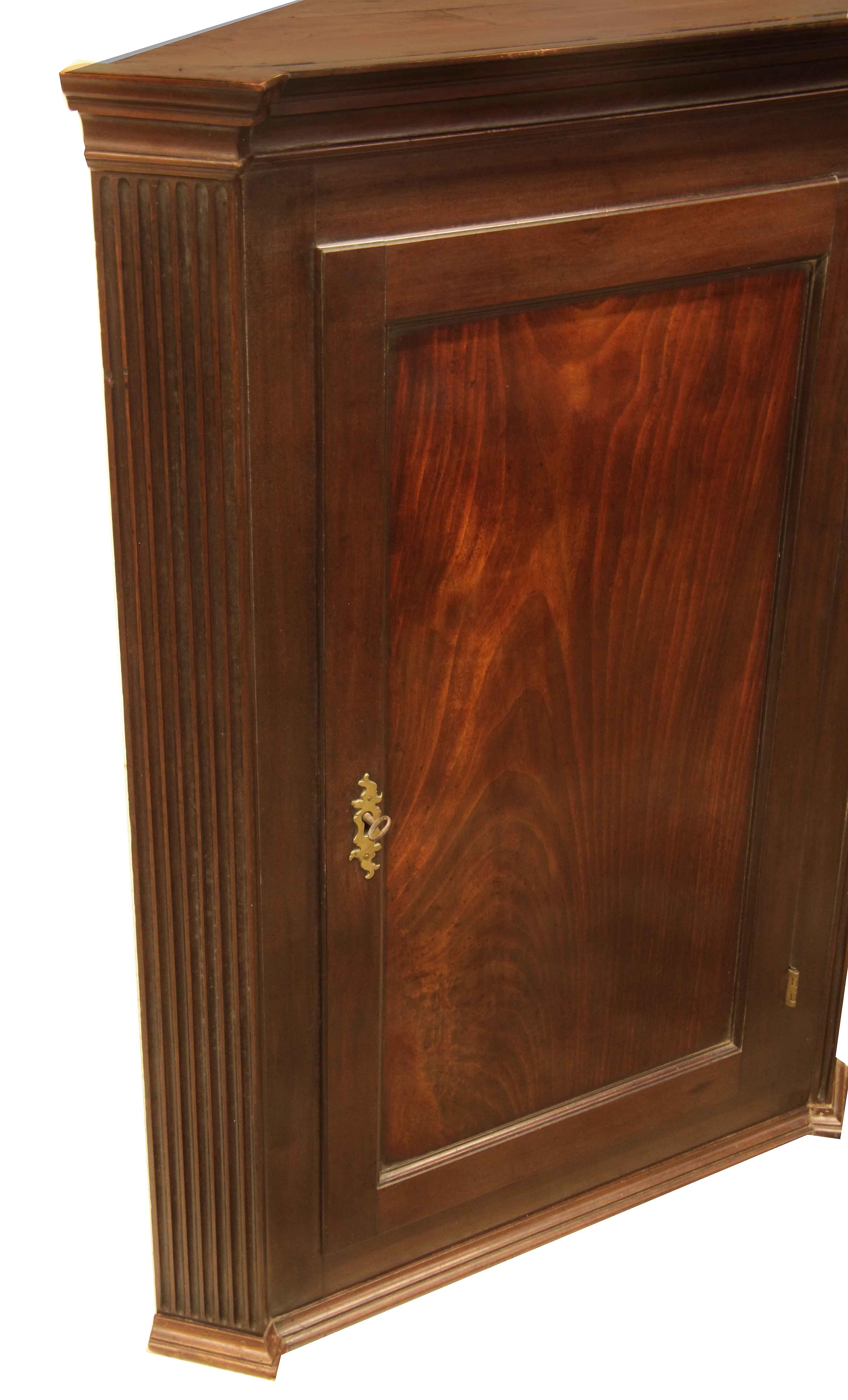 George III hanging corner cupboard, with cove cornice; the returns are blocked out and reeded , the door has a beautiful figured mahogany panel with excellent patina and color, original working lock and key. The interior features three shaped