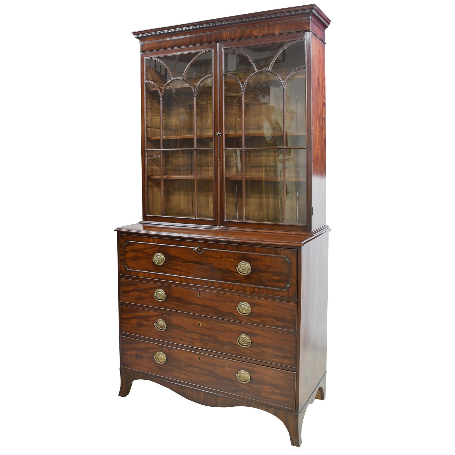 A stately George III secretary bookcase in fine, figured mahogany with inlaid mahogany banding on pull-out, drawer-front secretary. England, circa 1810. Bookcase is set back & has three adjustable shelves, with glazed doors that are decorated with a