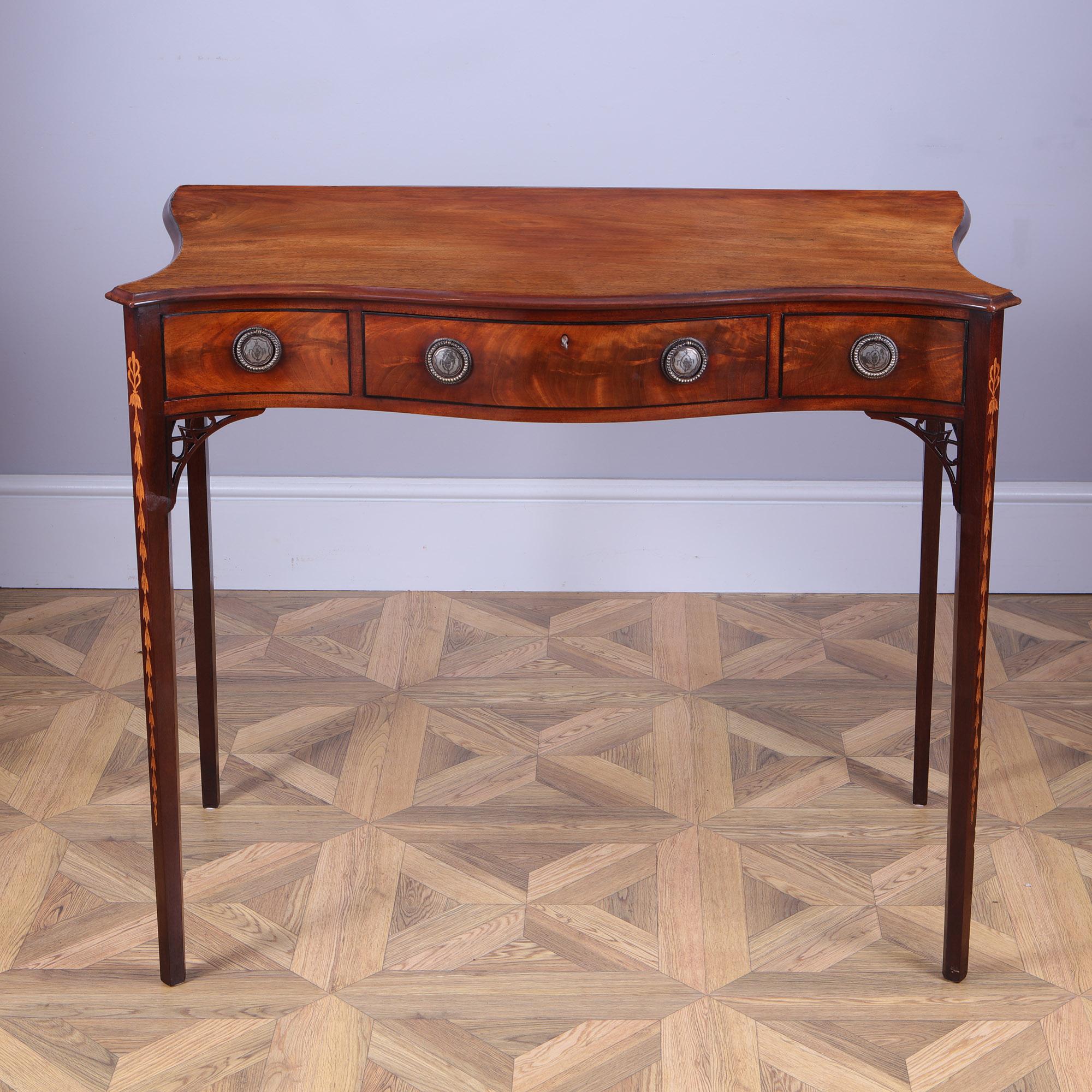 George III Hepplewhite Side Table, the well-figured solid mahogany top with the serpentine front and curved sides, above a frieze of three drawers, each with silver plated and engraved ring handles and a lock and key to the center. The whole raised