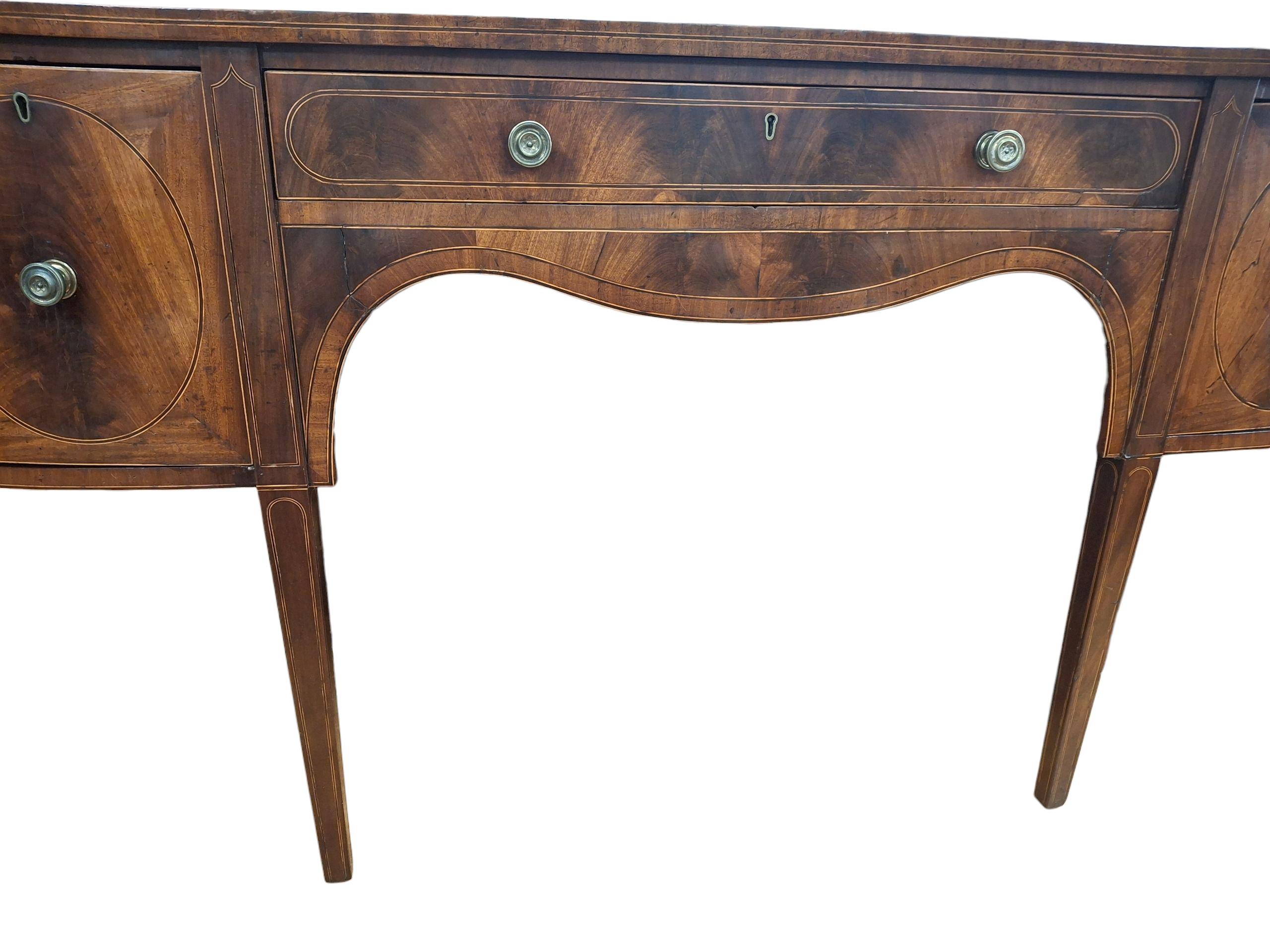 Credenza demi-lune in mogano intarsiato di Giorgio III.  Cassetto centrale anteriore sopra il grembiule a serpentina, due cassetti profondi e due armadietti laterali.  Poggia su quattro gambe affusolate.
Piccole riparazioni all'impiallacciatura del