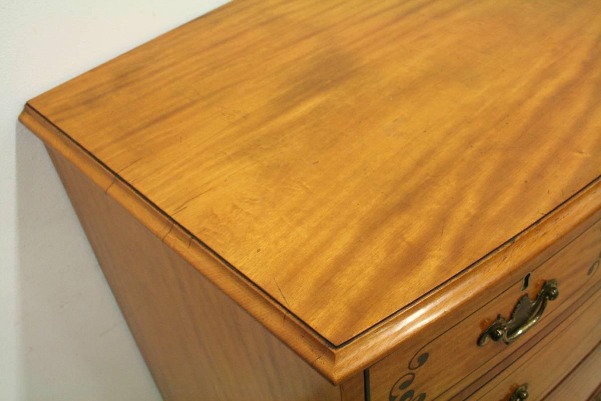 George III inlaid satinwood bow front chest of drawers, with three short above three long graduating drawers with elaborate scrolling ebony inlay and banded edges, and old (not original) brass handles, circa 1800. Standing on original French bracket