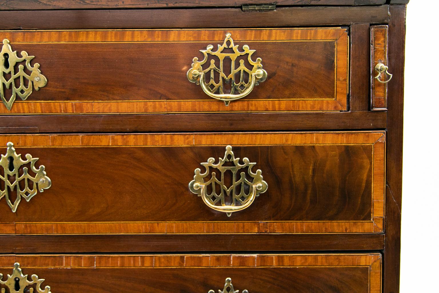 George III inlaid slant top desk, the top and fall board crossbanded with satinwood and ebony, the fall board also inlaid with quarter fans and shell, the drawers are also banded with satinwood and ebony. Trellis brasses are original.
  
