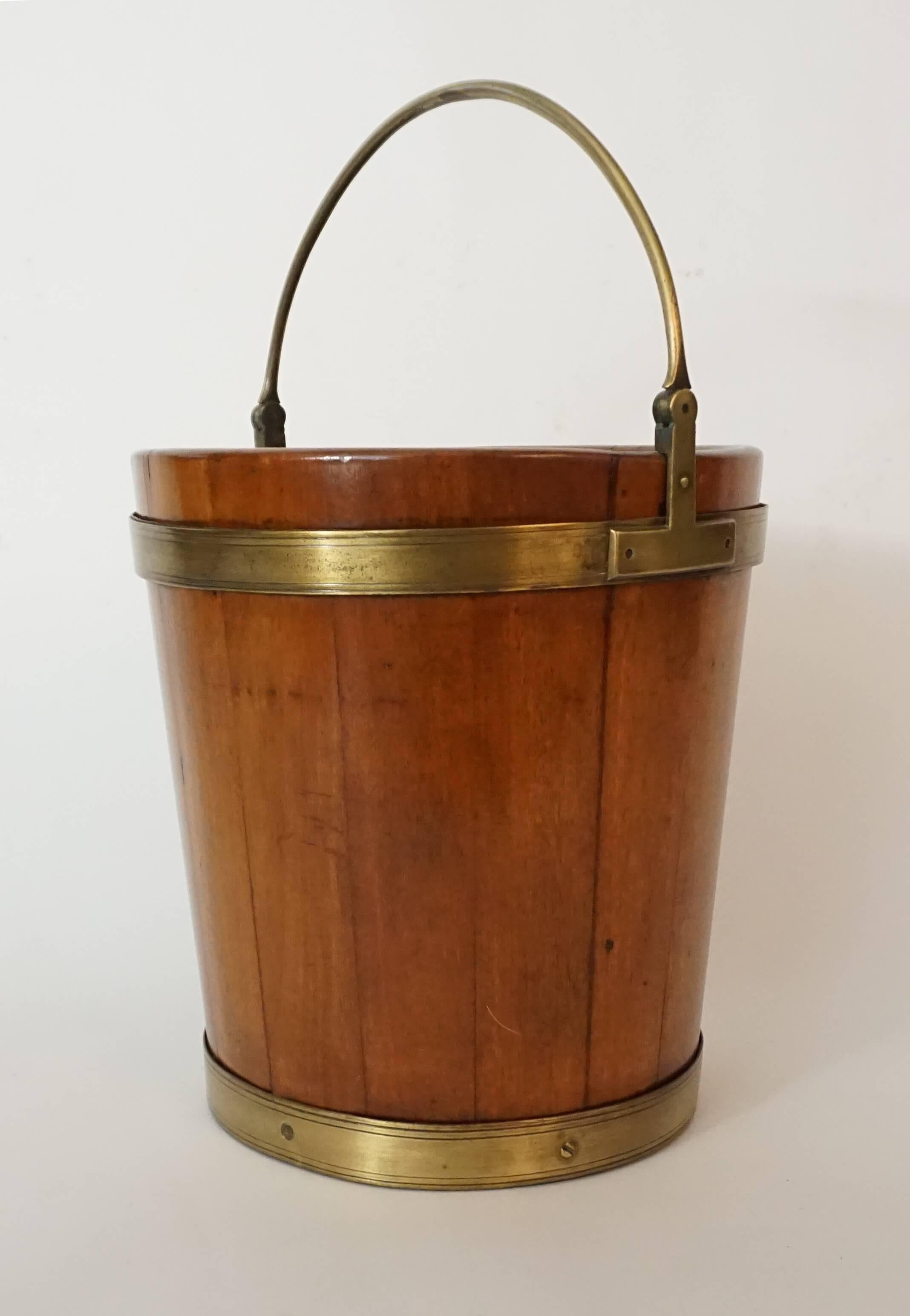 Irish George III circa 1780 peat, turf, or kindling bucket of solid blonde mahogany stave construction and round tapering form with brass banding and pivoting handle. Measurements: 25