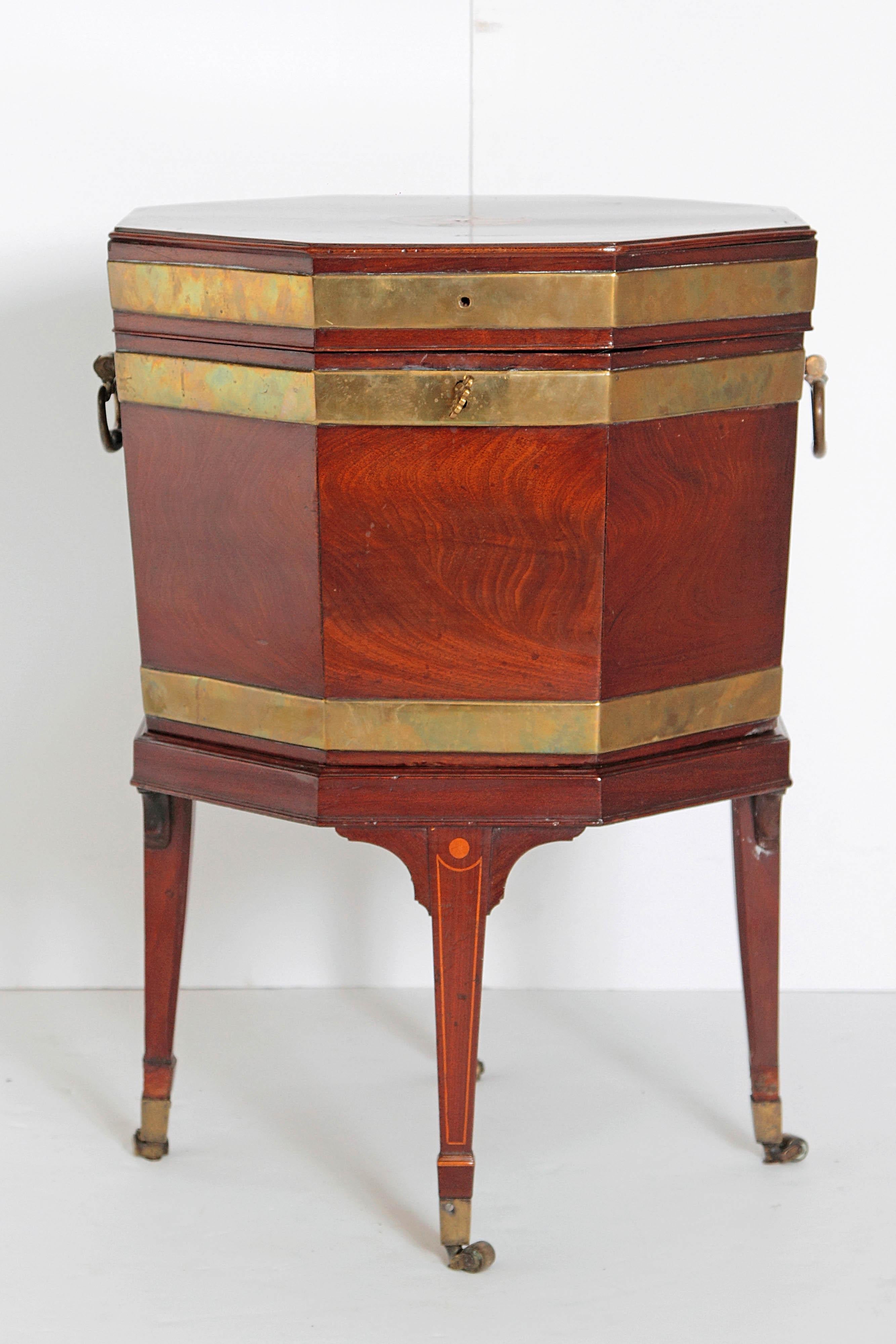 A George III brass bound mahogany octagonal cellarette/wine cooler on satinwood line inlaid tapering supports terminating in brass cups and casters. The octagon shape gives this piece its rare uniqueness, along with the brass bands, the large drop