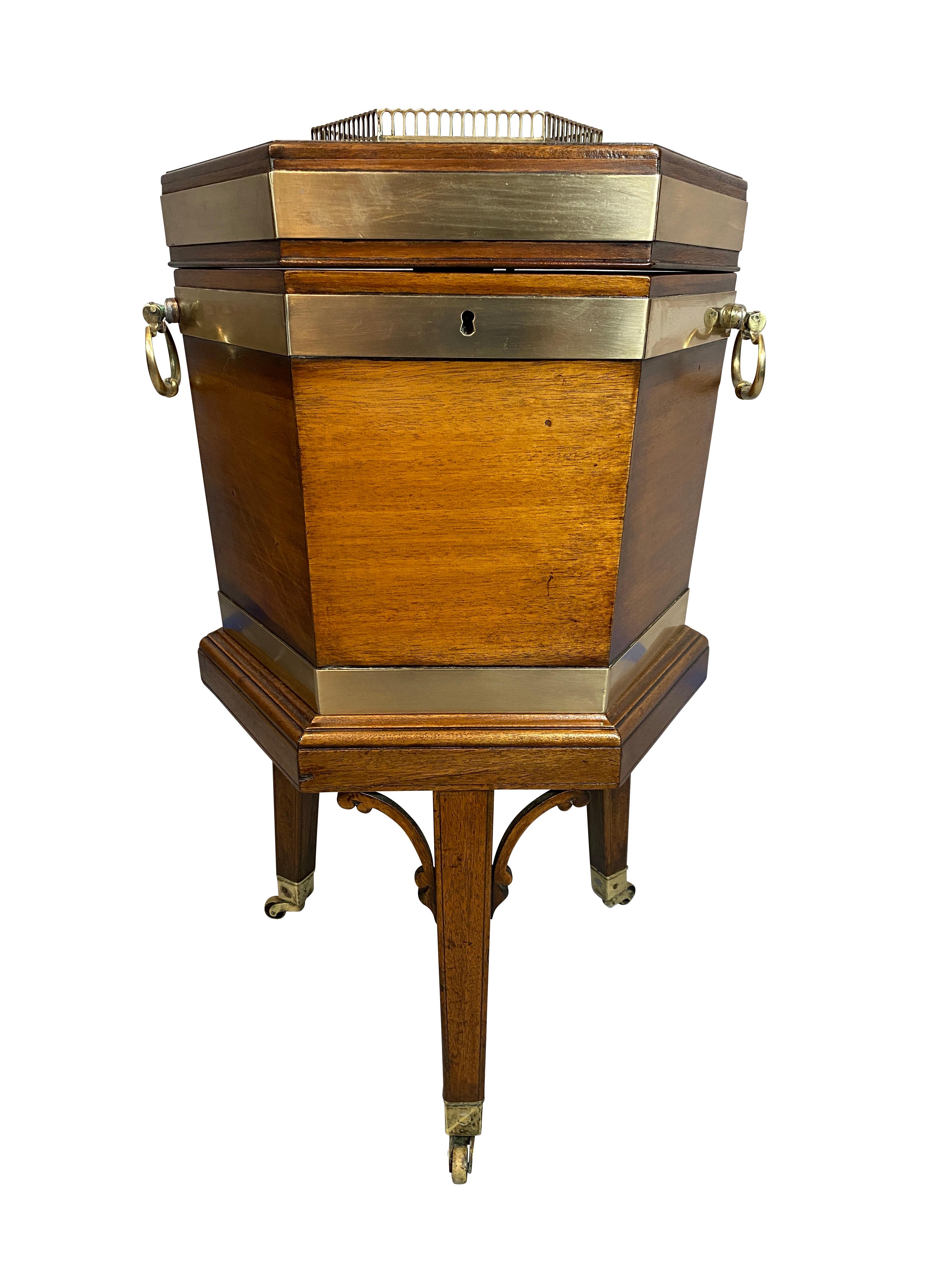Hexagonal hinged lid with brass gallery over a conforming case, the interior fitted for bottles, sides with brass strapping and carry handles, raised on square tapered legs with spandrels and ending on casters.