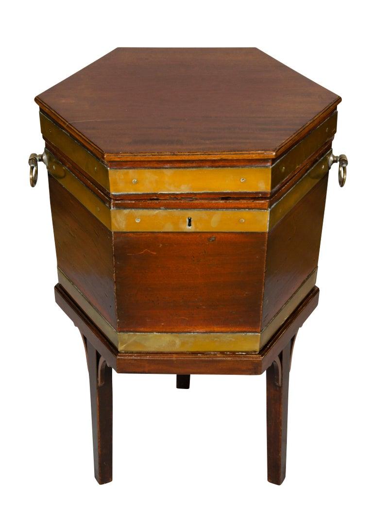 Hexagonal hinged top with lead lined interior, conforming case with brass strapping, raised on square tapered legs with spandrels at top of legs.