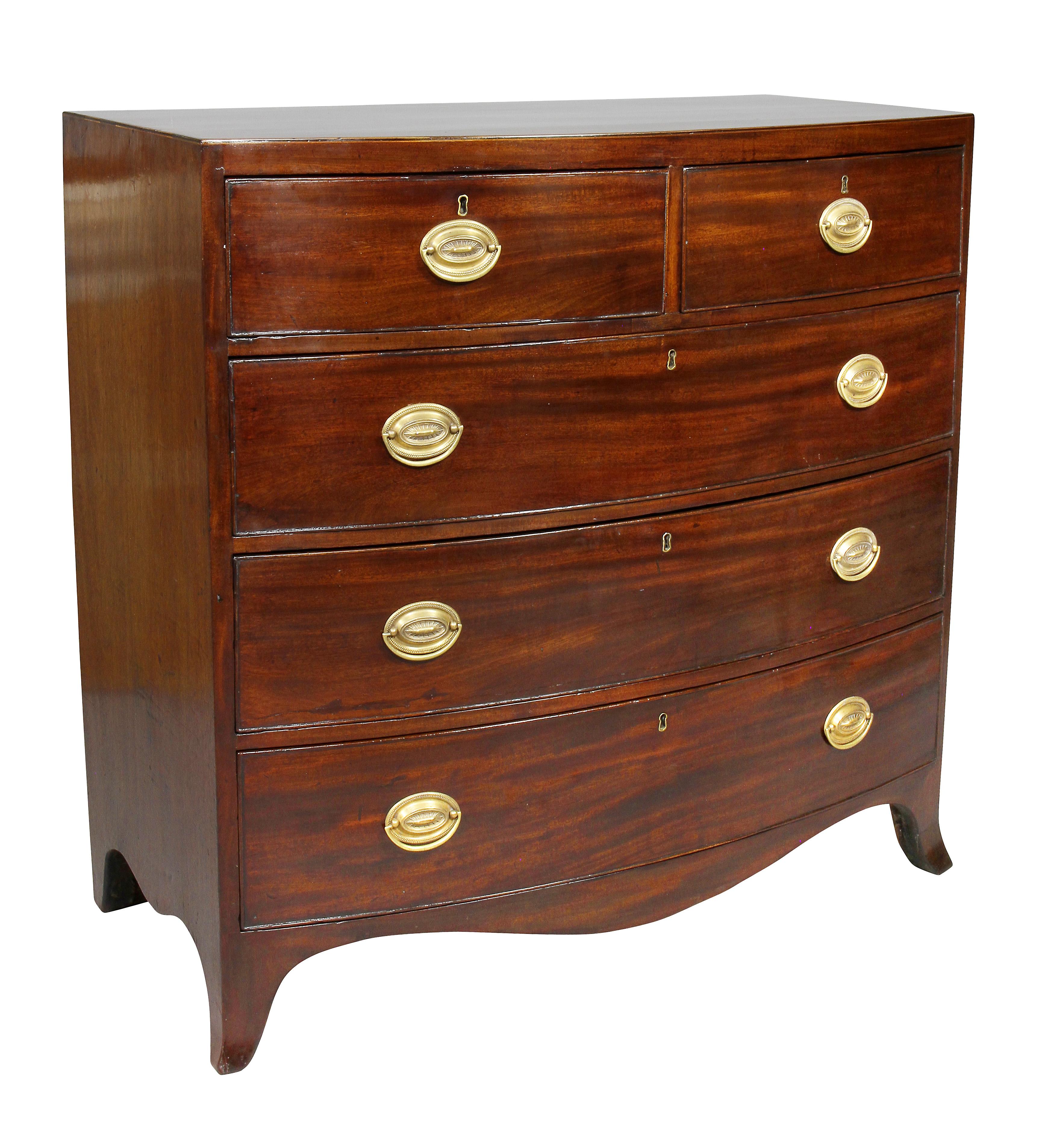 With rectangular bowed top over two over three graduated drawers, all with oval brass handles, splayed bracket feet.