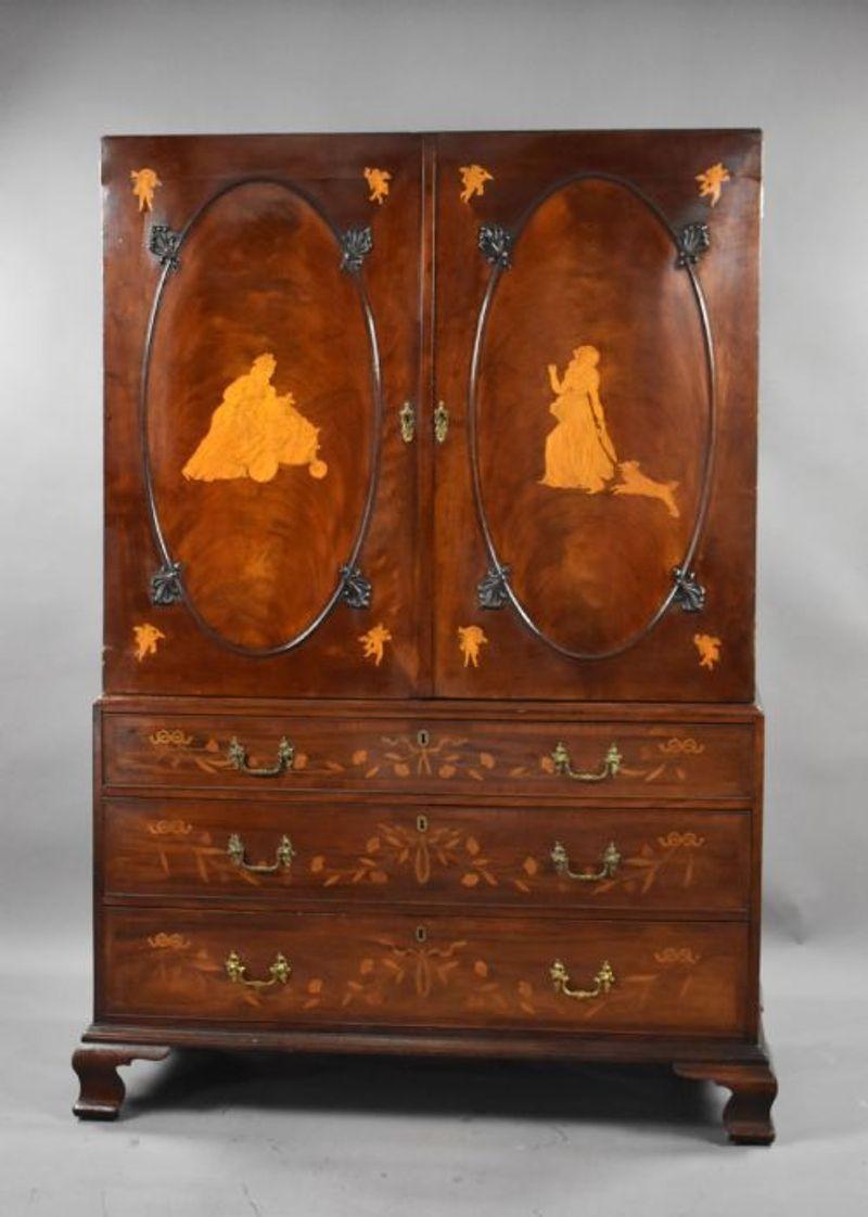 For sale is a top quality George III mahogany and inlaid clothes press in the manner of Ince & Mayhew. The inlay to the oval panel doors inlaid depicting putto and 18th century maidens, the doors opening to four sliding trays, the drawers to the