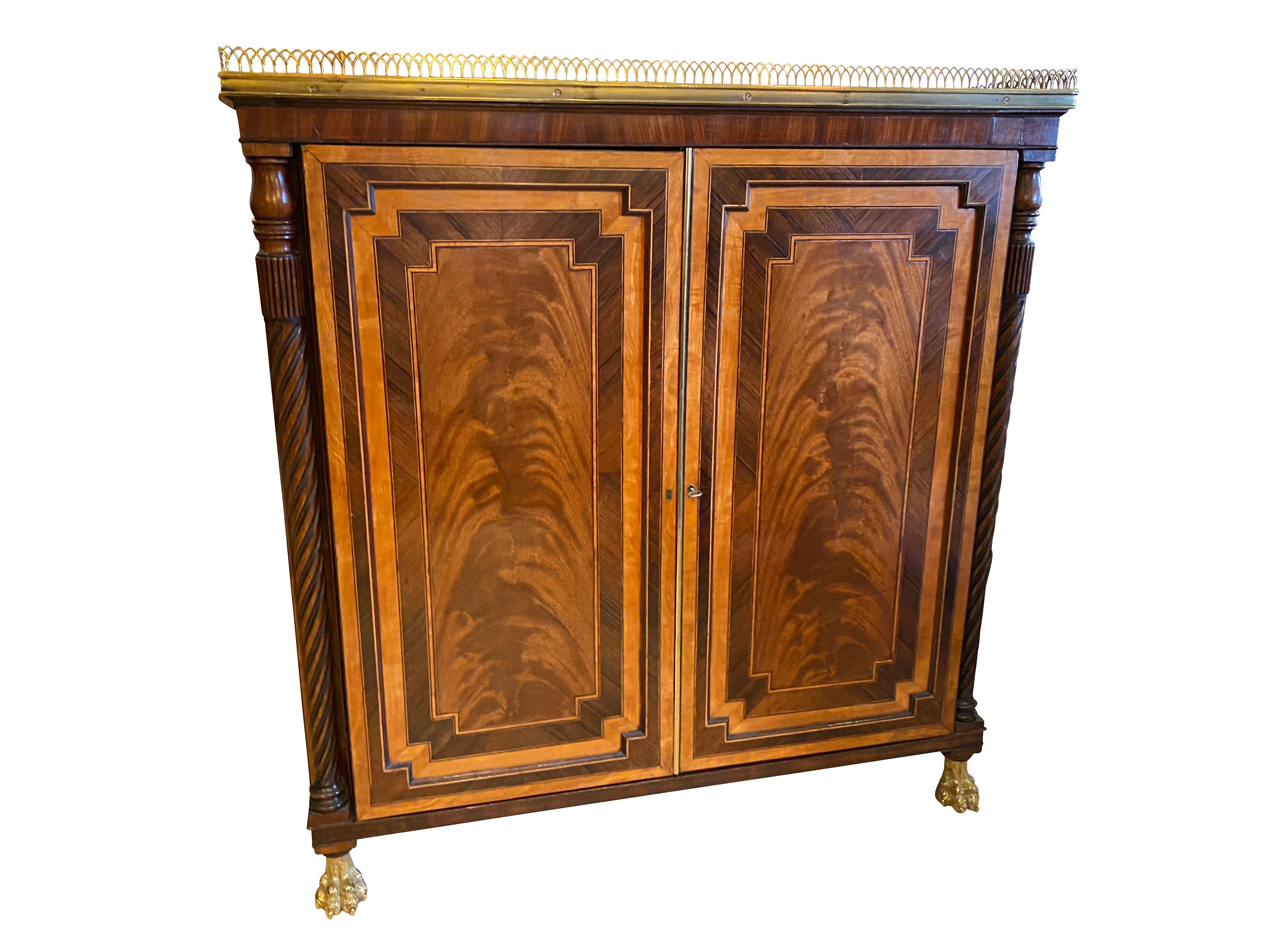 Finely constructed with choice veneers with crossbanded top with brass 3/4 gallery over a pair of paneled doors with a pair of opposing doors with pleated fabric, each corner with reeded columns, brass paw feet.