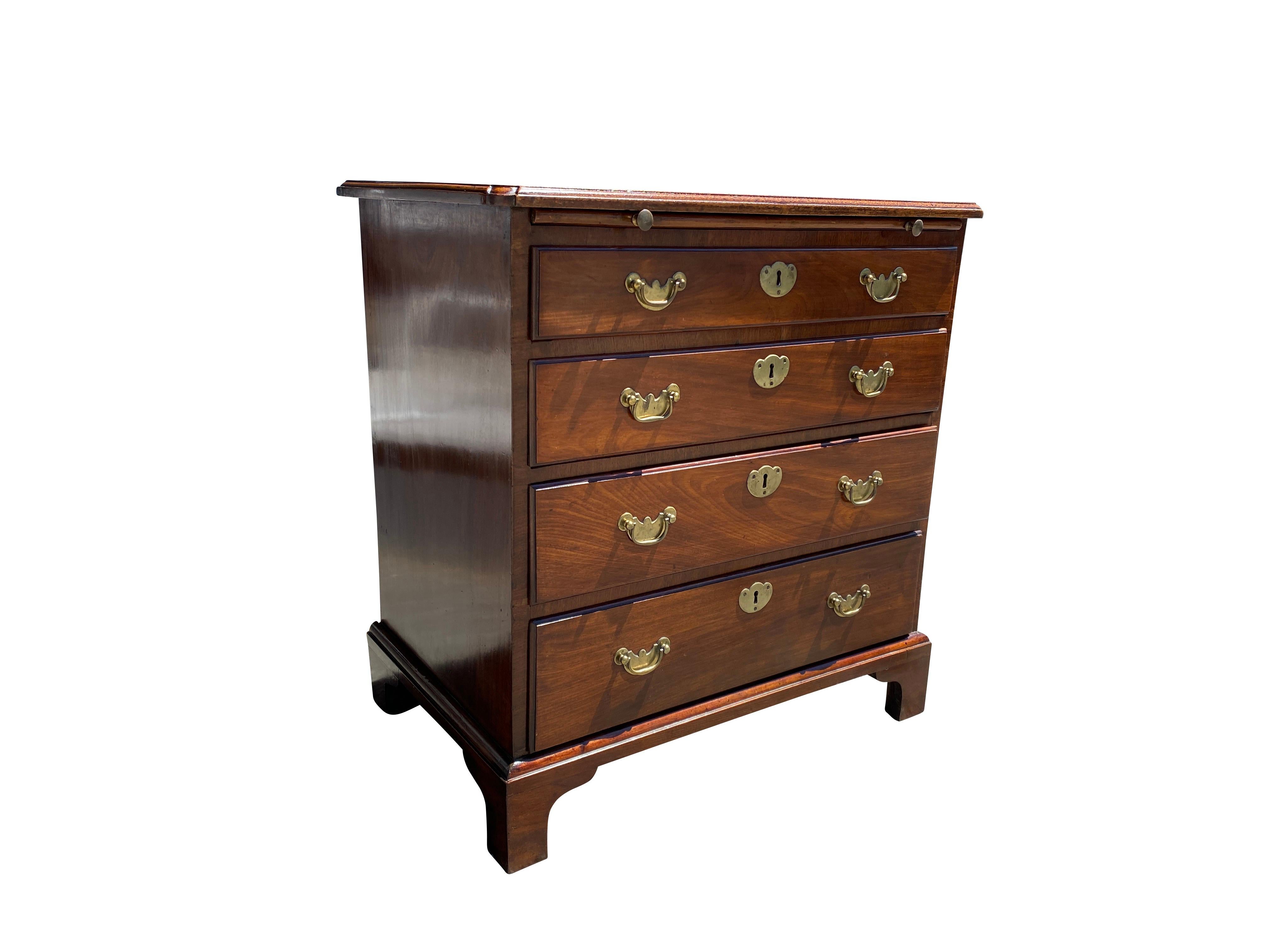 Rectangular top with molded corners and edge, with brushing slide over four graduated drawers. Brass bail handles. Bracket feet.