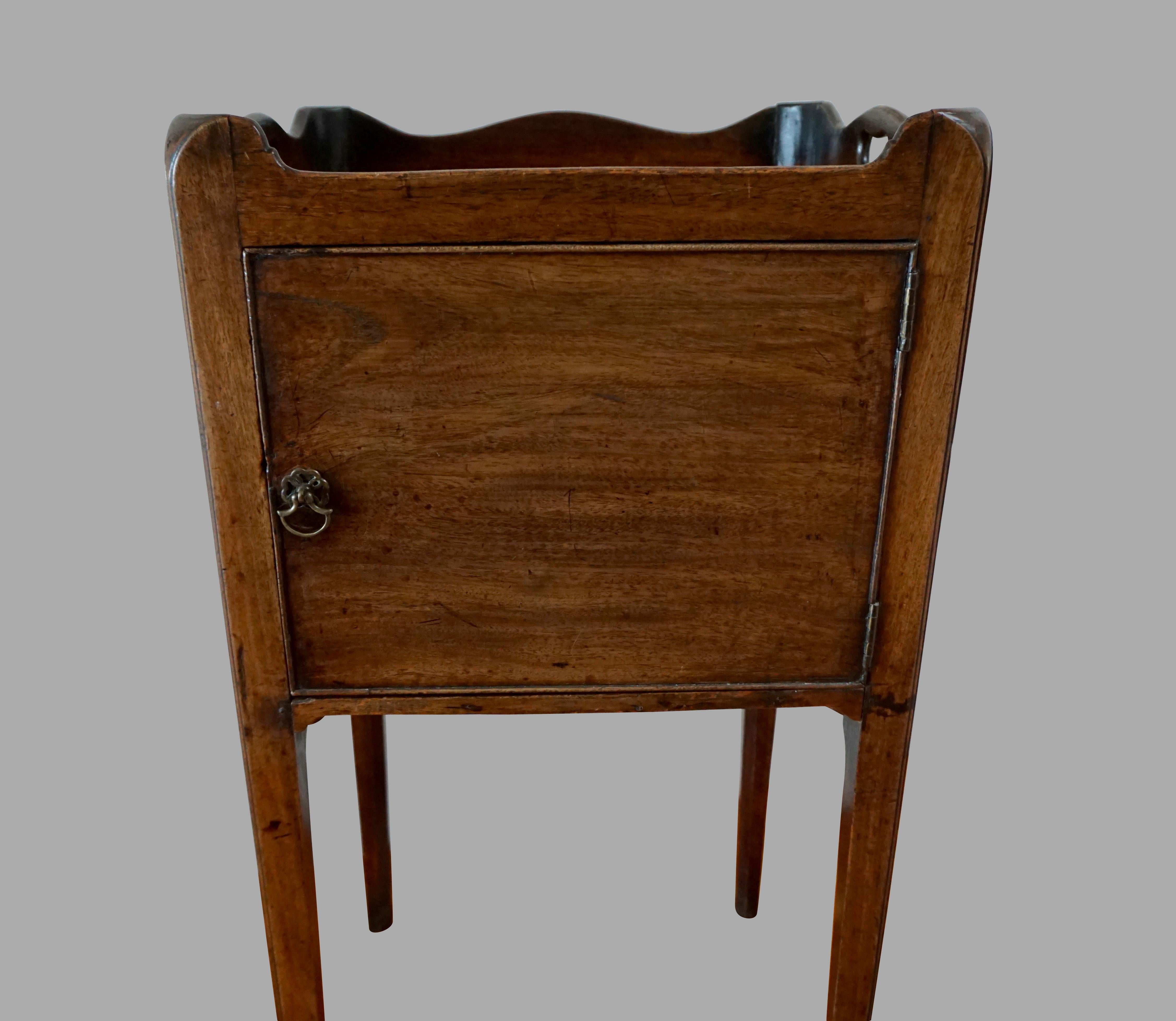 An English George III period mahogany bedside commode, the shaped gallery top with cutout handles above a cupboard door, supported on square tapered legs. Provenance: H.W. Keil Ltd. Tudor House, Broadway, Worcestershire U.K. Purchased 1985. Circa