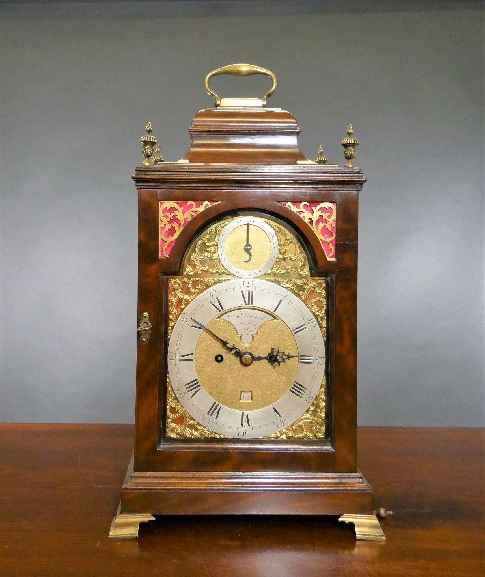 George III bracket clock by Paul Rimbault, London
 
Finely figured mahogany bell top case with four finials surmounted by a brass hinged carrying handle standing on a stepped, raised plinth and resting on four outswept brass bracket feet. Cast