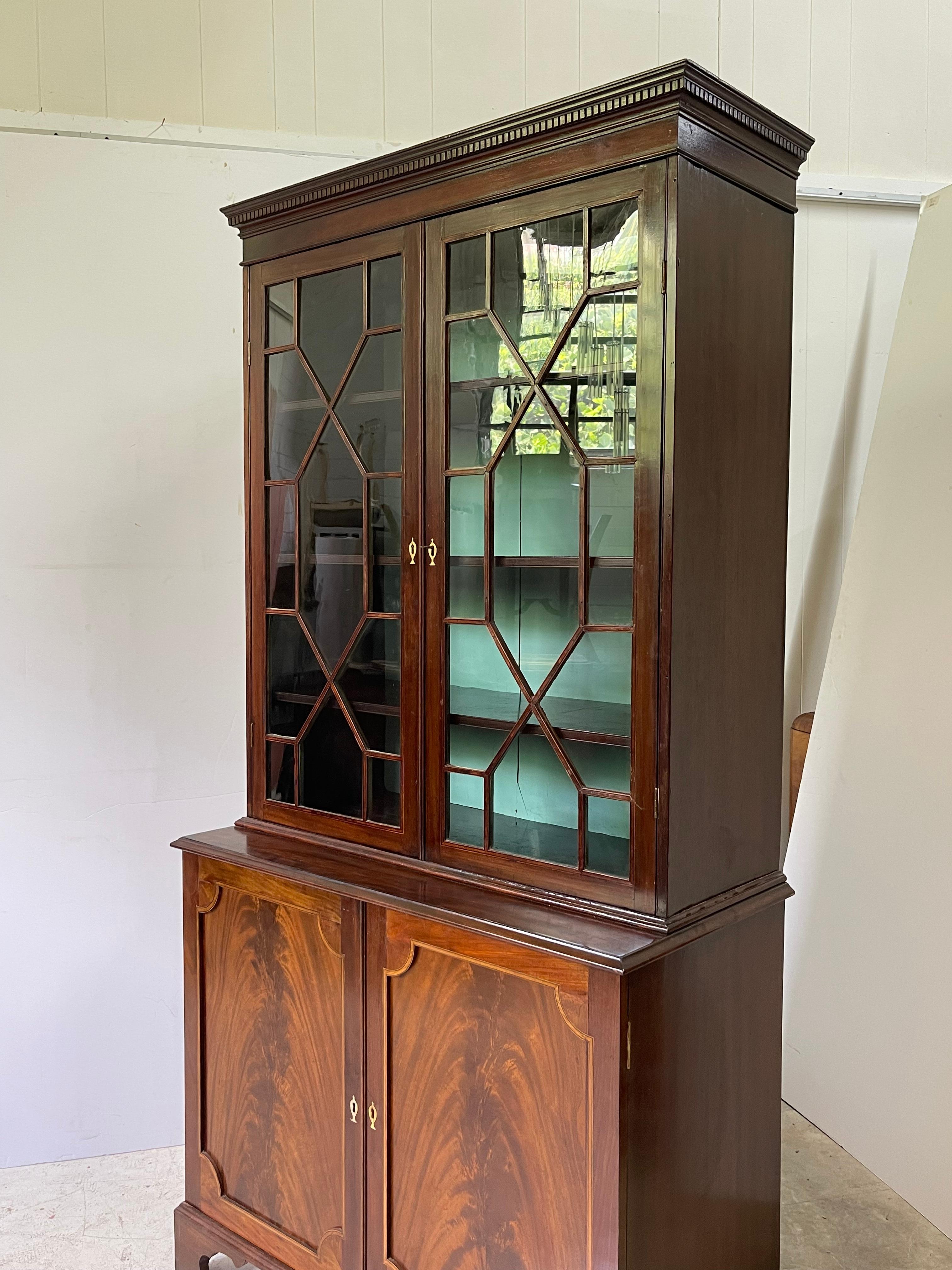 An English late George III period bookcase made of flame mahogany with fine satinwood inlay. The upper section has an elegant cornice with dentil moldings over a pair of glazed doors with an astragal bar. The interior is fitted with three solid