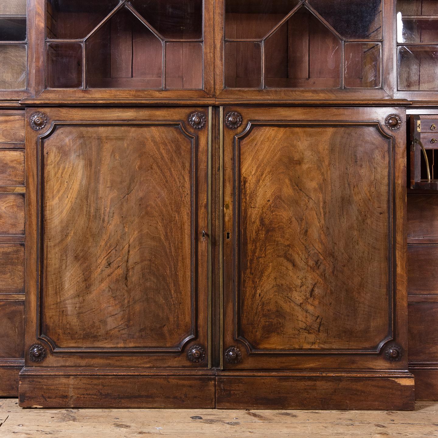 A George III mahogany bookcase, of breakfront form, the dentil cornice and fluted frieze above astragal glazed doors enclosing adjustable shelving, the base with cupboard flanked by graduated drawers , one side with secretaire, on plinth base.

A