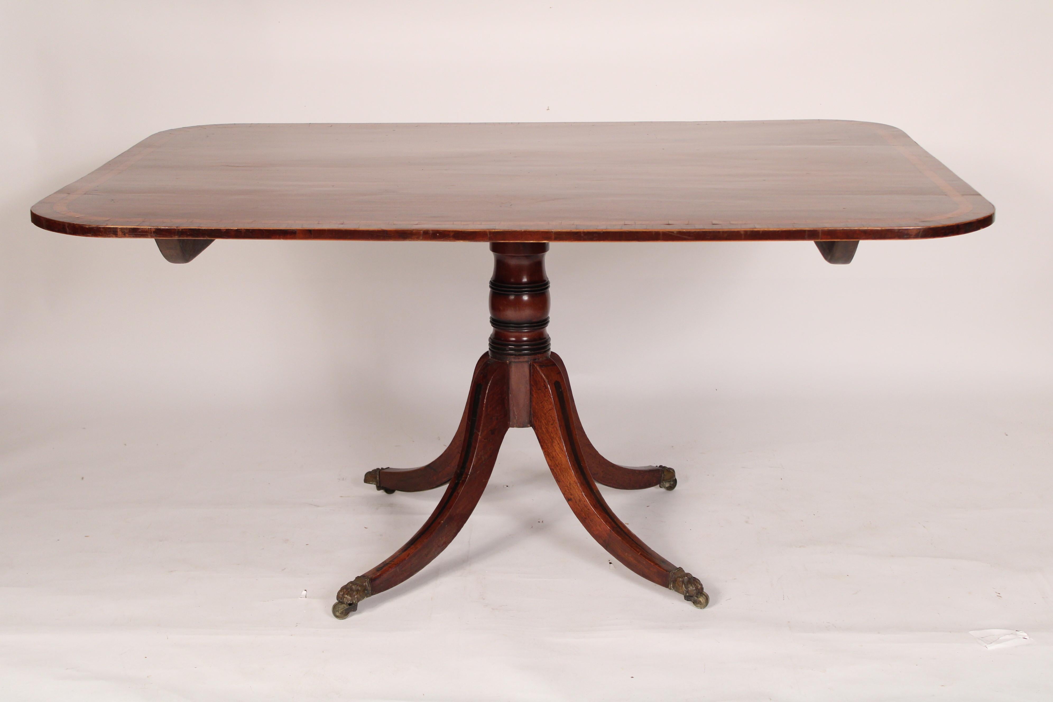George III mahogany breakfast table, circa 1800. Mahogany top with rosewood and satinwood cross banding, a turned mahogany pedestal with 4 down swept mahogany legs with ebonized inlay, the legs ending in brass paw feet. Knee clearance 28.25