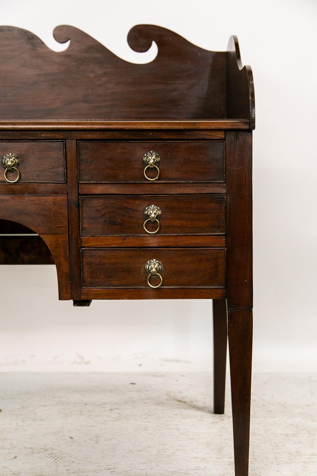 This buffet/server has a three-sided gallery and a shaped crest with a breaking wave motif. The top front edge has a bullnose molding above seven drawers with the original lion's head pulls. The center has an arched apron supporting the middle
