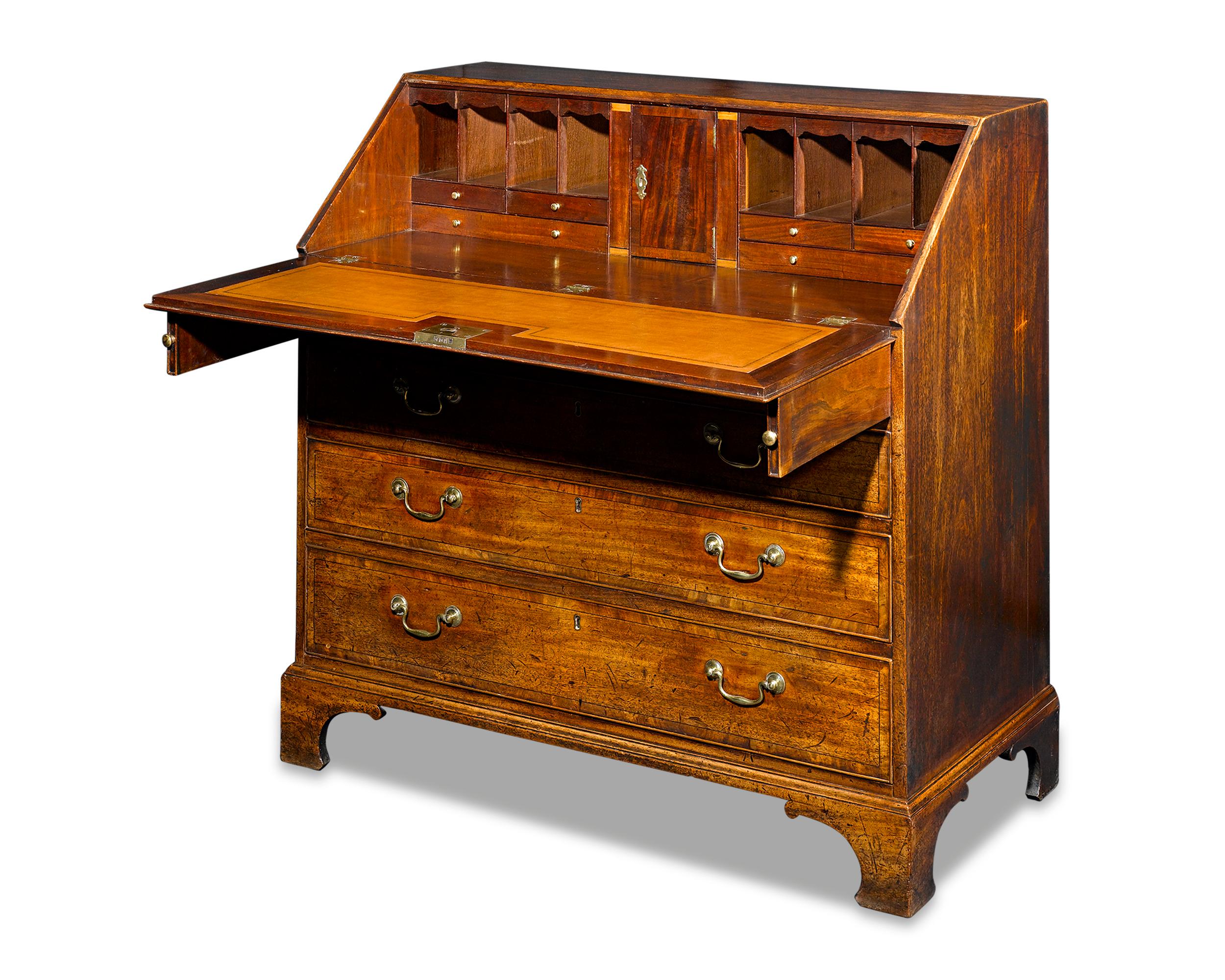 This classic bureau writing desk is a brilliant specimen of Georgian furniture. Crafted of mahogany that has aged to a rich patina, this desk features a drop-front writing desk that opens to reveal a spacious surface and an array of compartments.