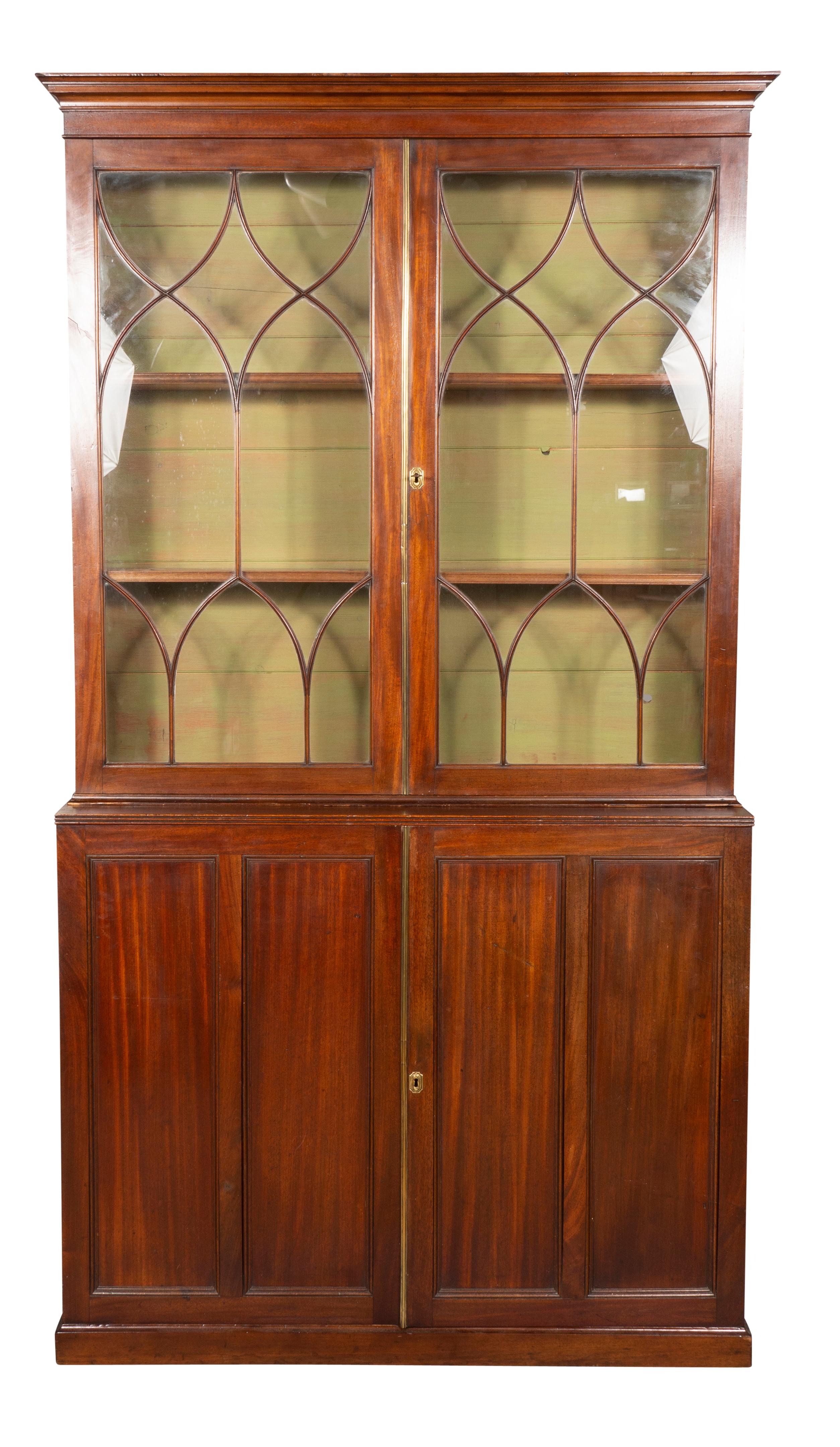 With a simple cornice over a pair of glazed doors with Gothic style mullions. Enclosing two adjustable shelves , the base with a pair of paneled doors enclosing three shelves. Raised on a plinth base. With key.