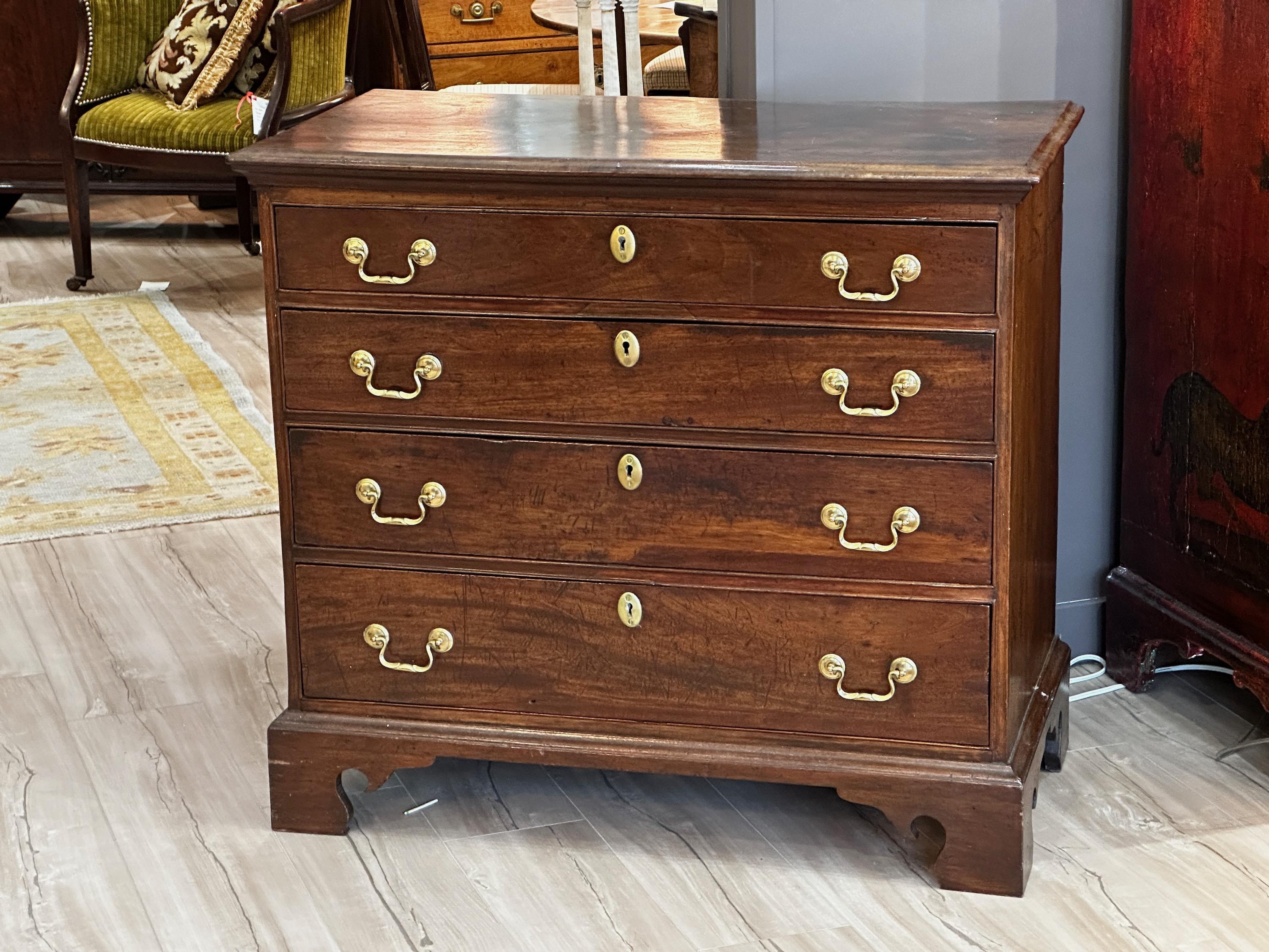A late 18th century small scale Georgian chest of drawers having four graduated drawers with original brass bail raised on shaped bracket feet. Mahogany is the primary wood with oak and pine as the secondary woods. No keys.