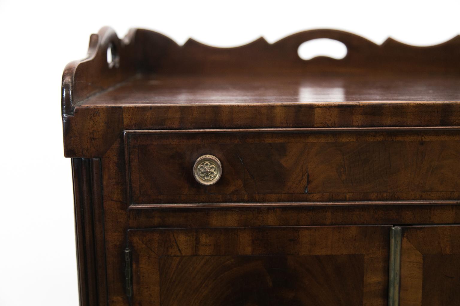 George III mahogany commode, with scalloped gallery, crotch mahogany doors, and drawers crossbanded with straight grain mahogany. It has reeded quarter columns that flank the doors and terminate in three quarter feet. The lower drawer has the