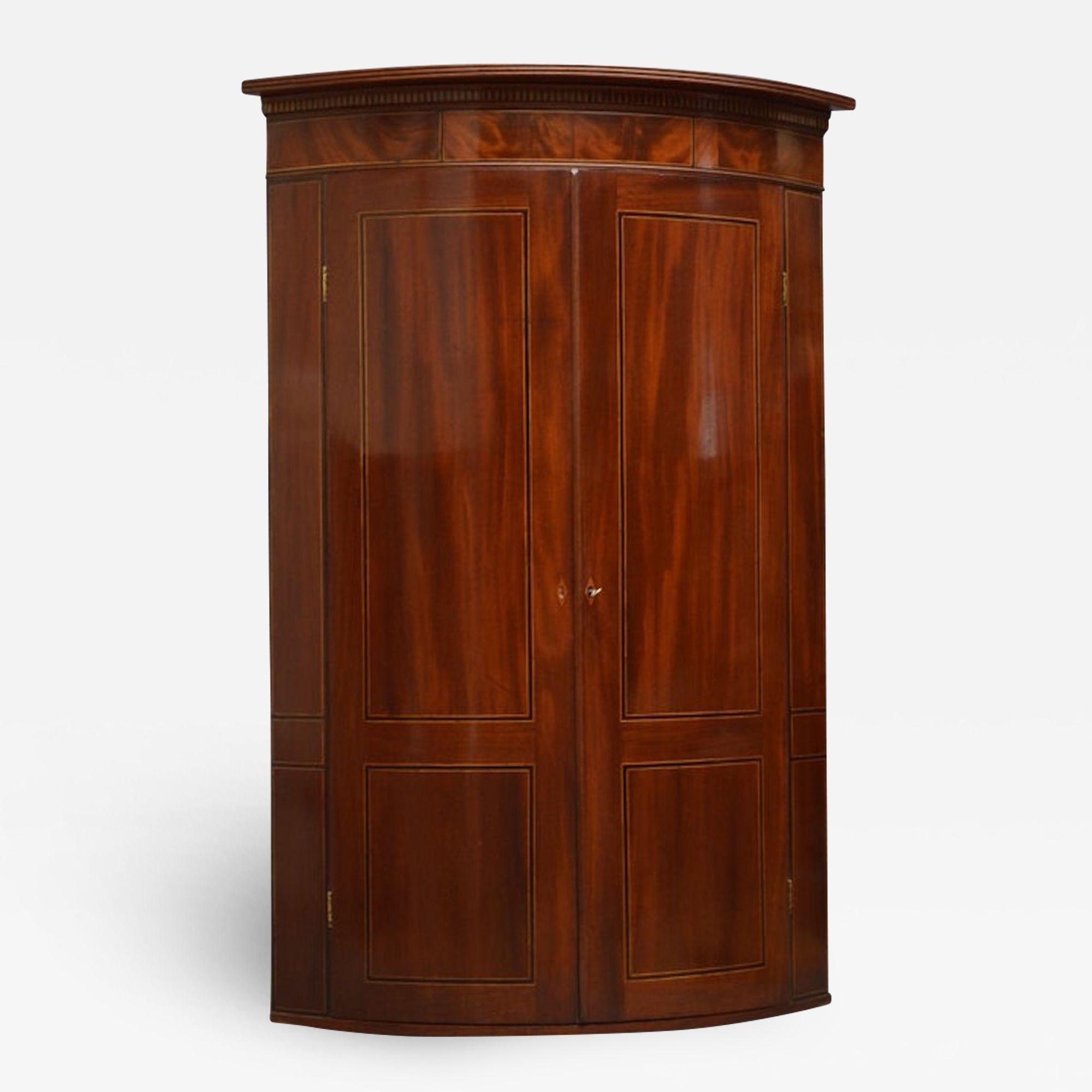 Sn3065 Fine example of Georgian, mahogany bowfronted corner cupboard, having reeded cornice with inlaid dentil decoration above string inlaid flamed mahogany frieze and a pair of ebony and satinwood string inlaid doors, enclosing 2 shelves and spice