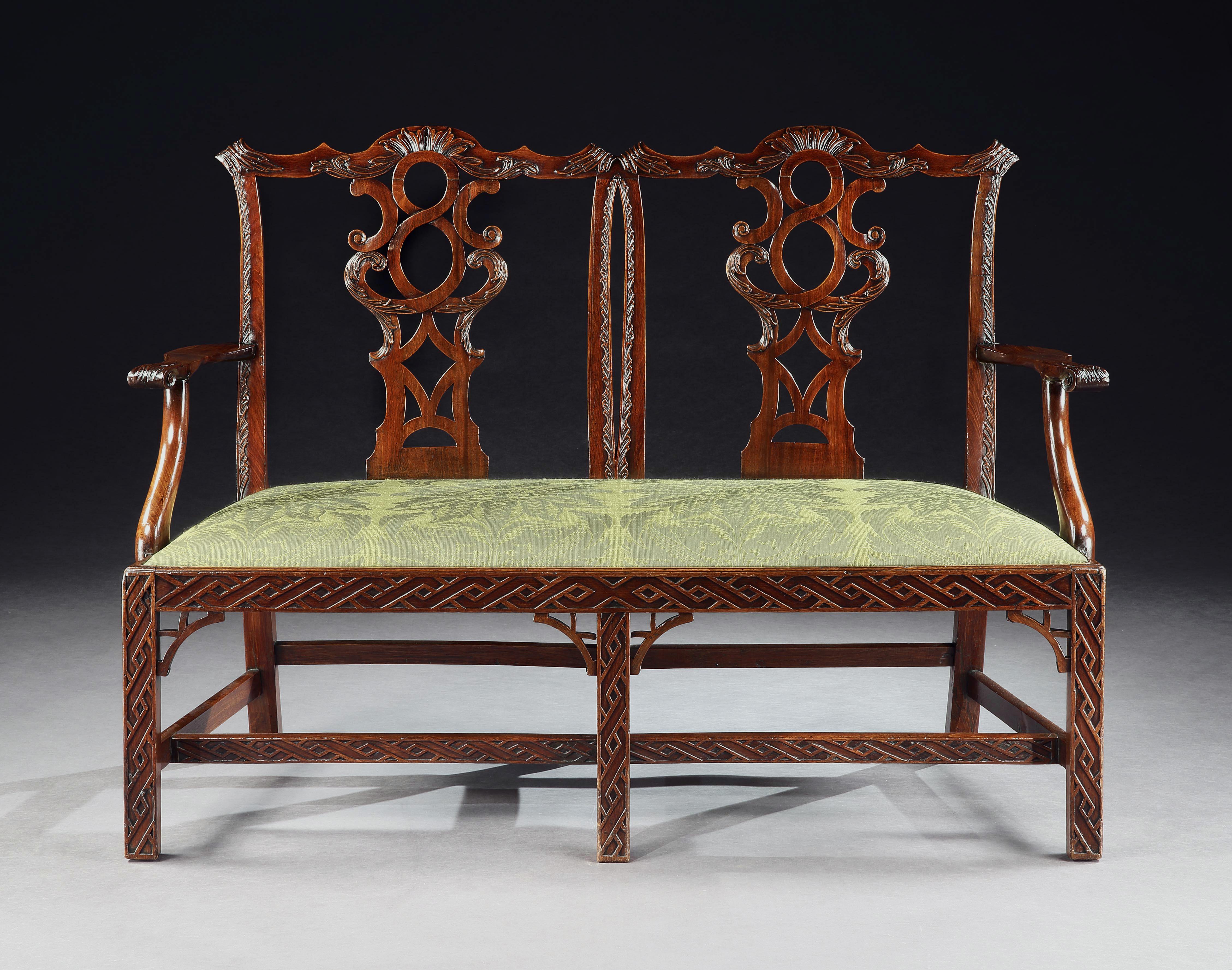 A fine mid-18th century Chippendale double chairback settee in mahogany with carved shaped top rails, pierced carved splats and outscrolling arms. The drop in seat covered in gold silk damask, the frieze and square chamfered legs decorated
