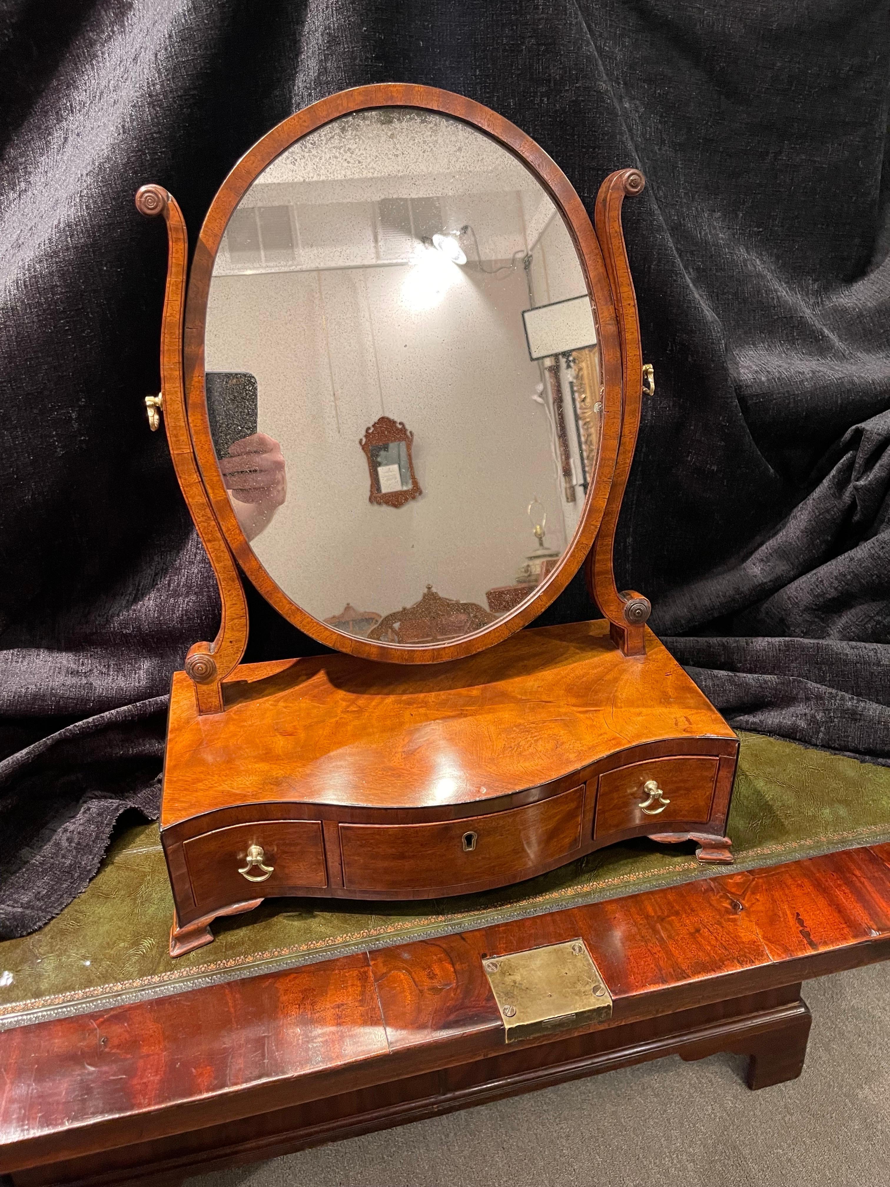 A lovely George III Mahogany dressing mirror, it’s oval mounted 
Above a serpentine case with 3 drawers raised on bracket feet. Brass 
Handles & keyhole escutcheon.